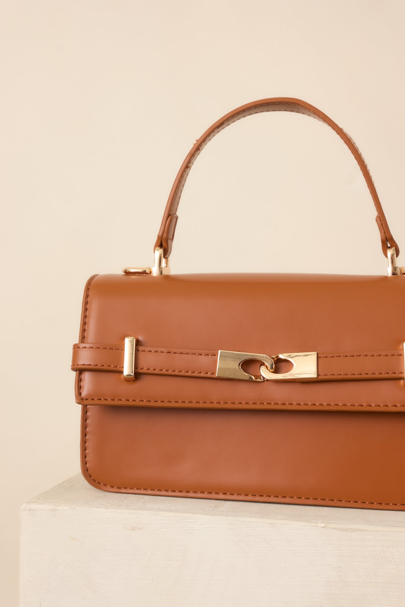 Close-up of the handbag’s front belt detail and polished gold-tone hardware against the smooth cognac faux leather exterior.
