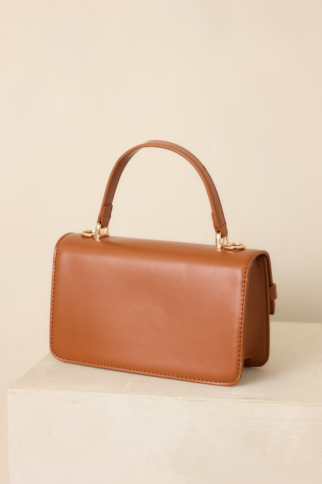 Rear view of the cognac faux leather handbag, showcasing its structured silhouette, smooth exterior, top handle, and clean back panel.