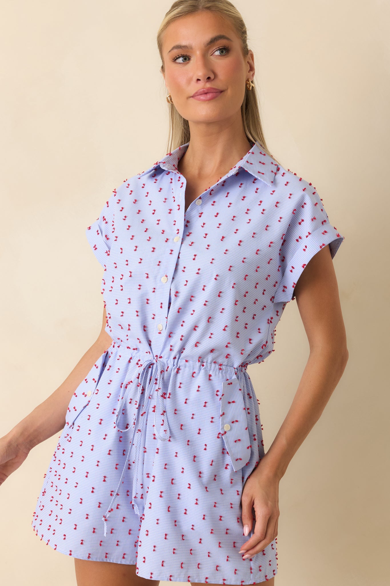 Collared gingham romper featuring rolled cap sleeves, functional pockets, and a playful embroidered finish.