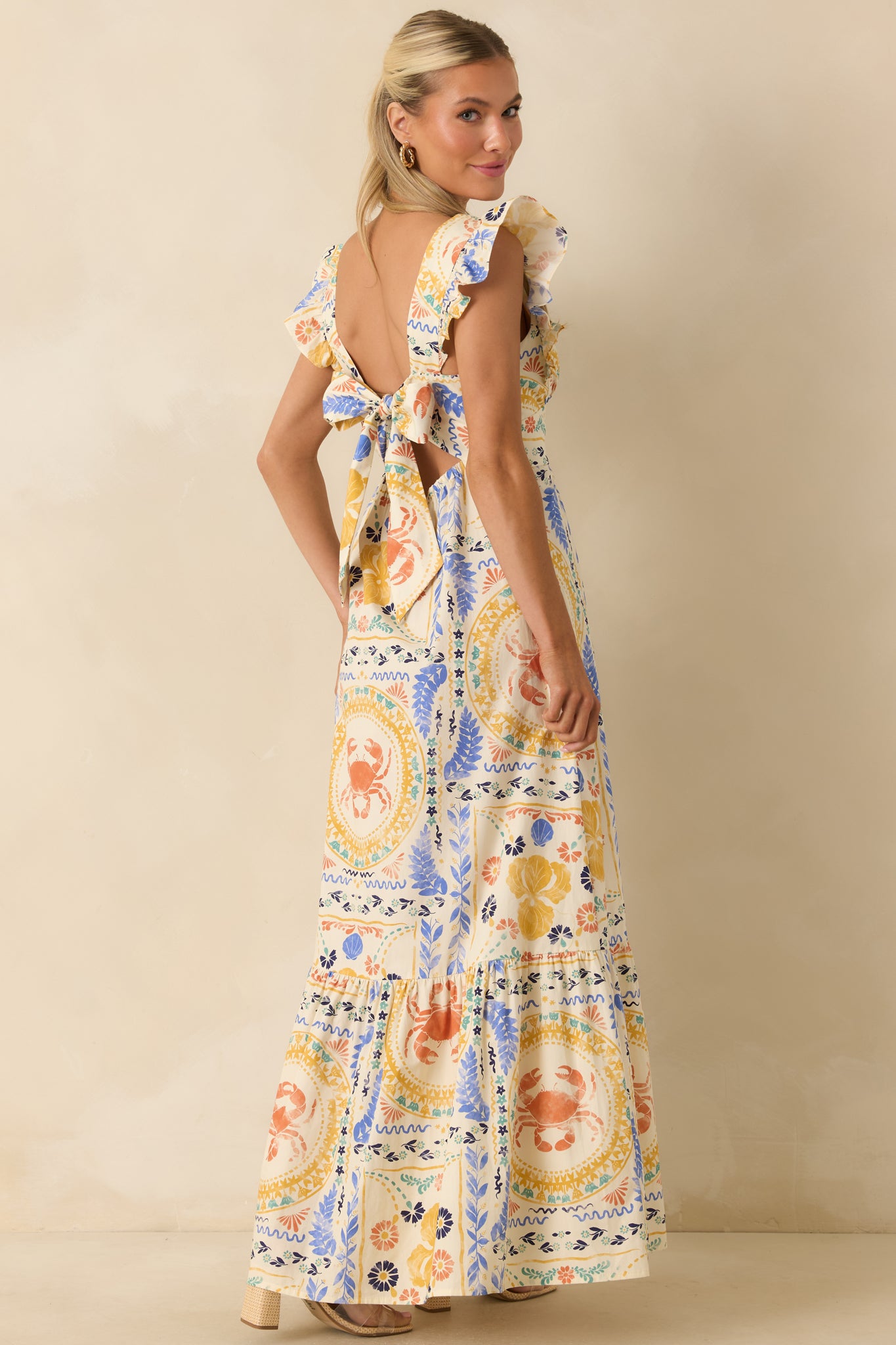 Rear view of the colorful maxi dress featuring a statement open back, oversized self-tie bow, ruffled cap sleeves, and flowing tiered skirt.