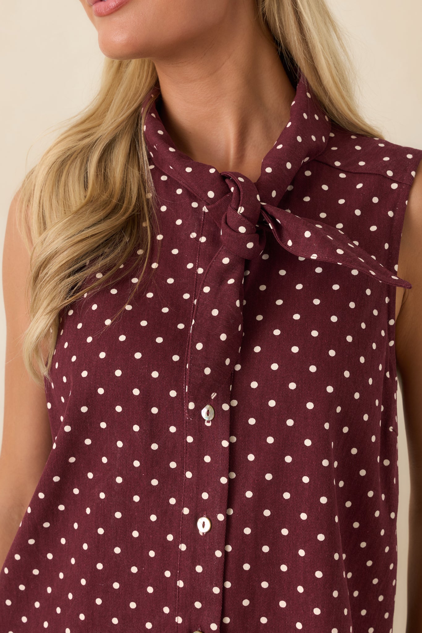 Close-up of the cotton mini dress highlighting the ivory polka dots, self-tie neckline, functional buttons, and textured fabric.