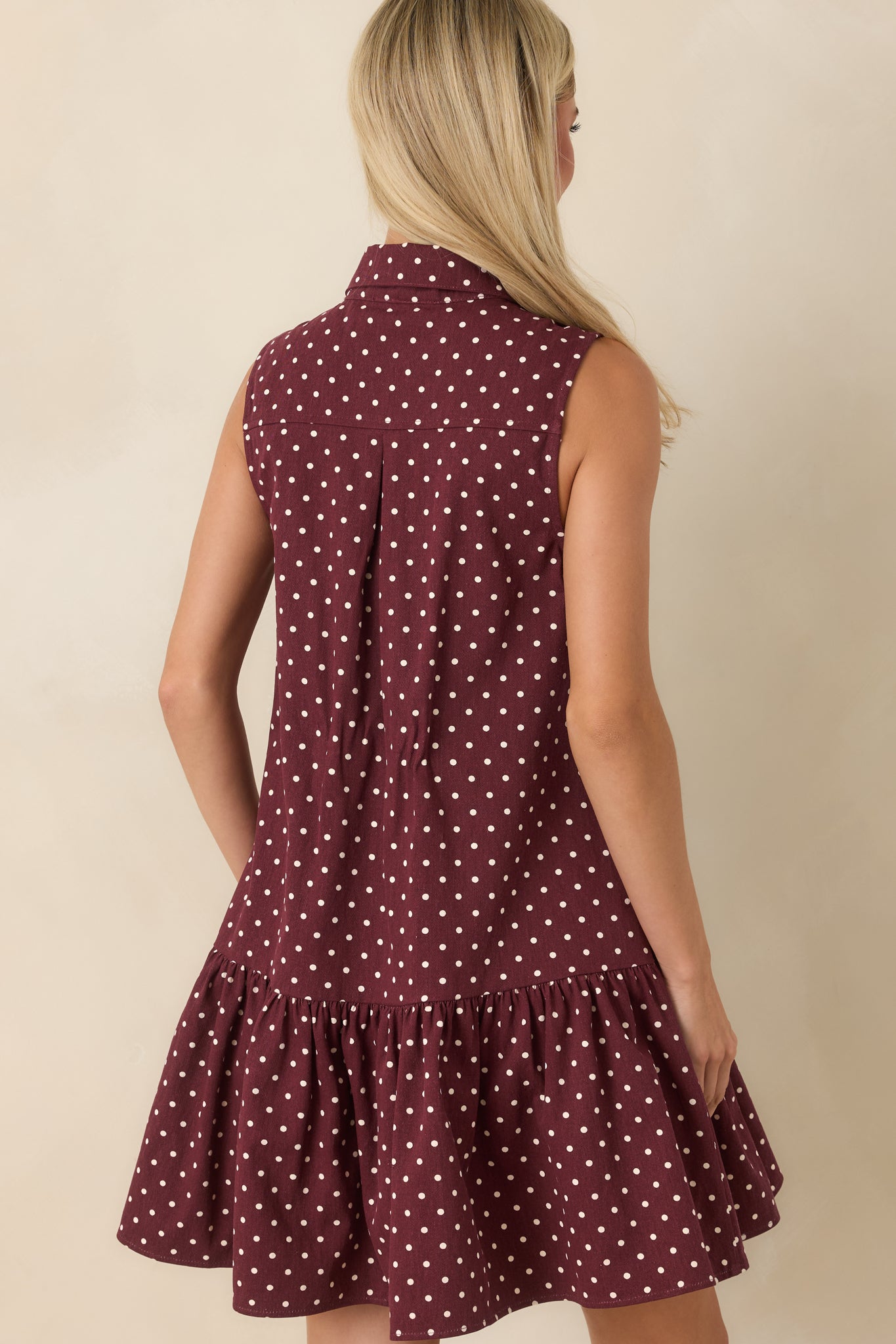 Rear view of the sleeveless cotton mini dress featuring a relaxed drop-waist silhouette, gathered ruffle hem, and ivory polka dot pattern.