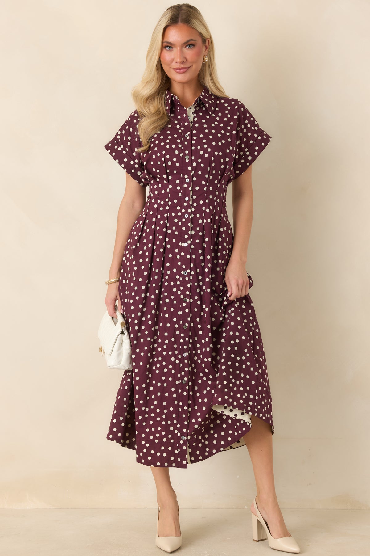 Fit-and-flare cotton midi dress with a collared neckline, short sleeves, full button placket, defined waist seams, and plum polka dot detailing.