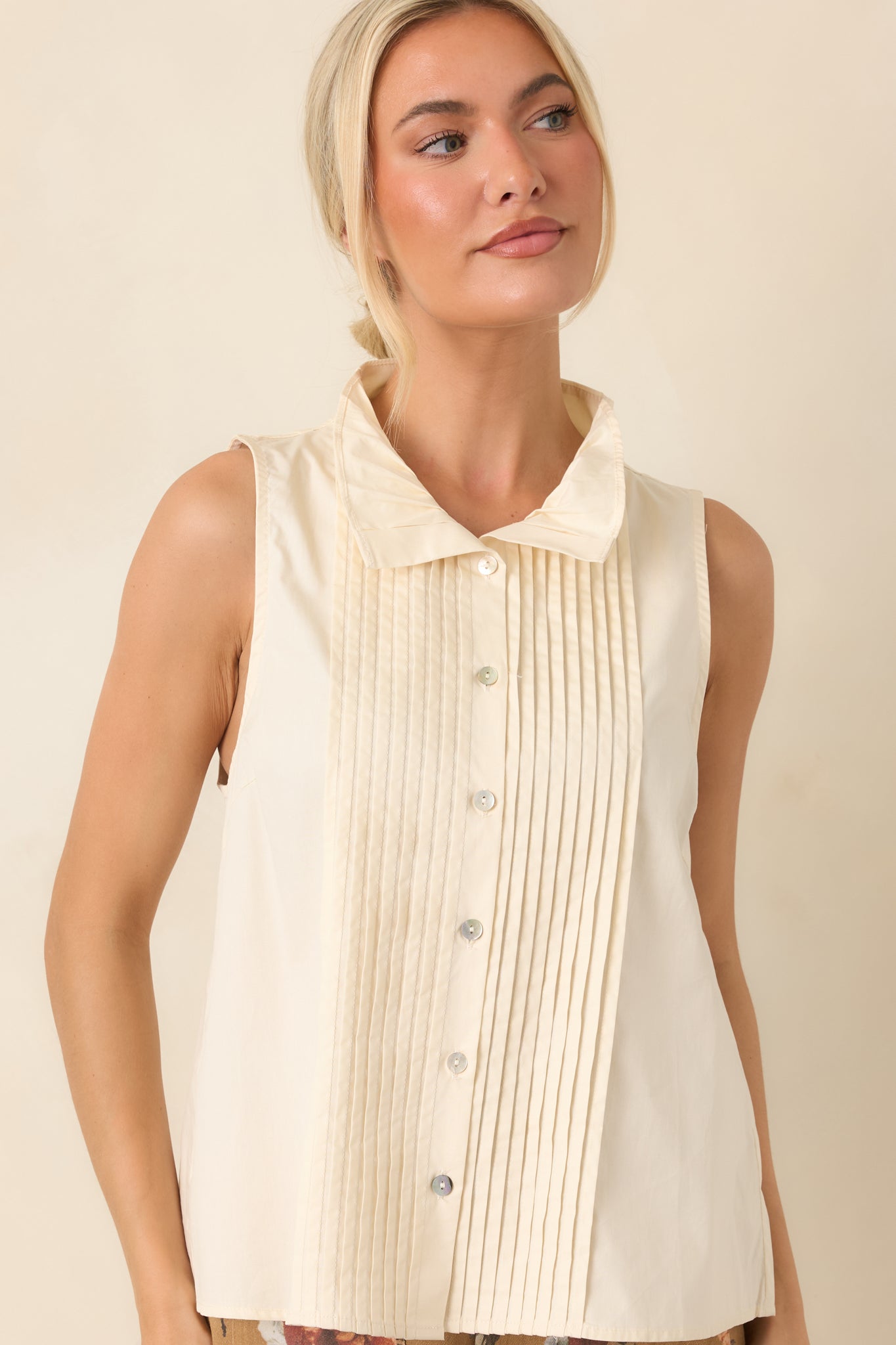 Cotton sleeveless blouse with a classic collar and crisp pleated accents that add subtle dimension and texture.