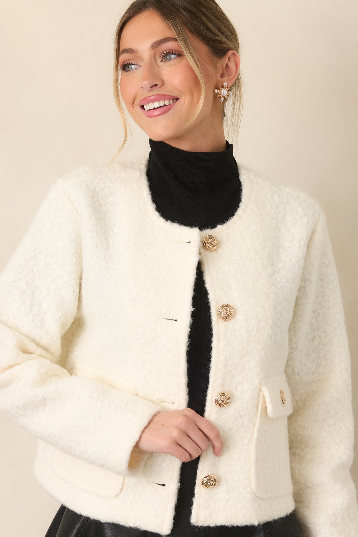 Close view of the textured cream bouclé fabric, front flap pocket, and gold button detailing.
