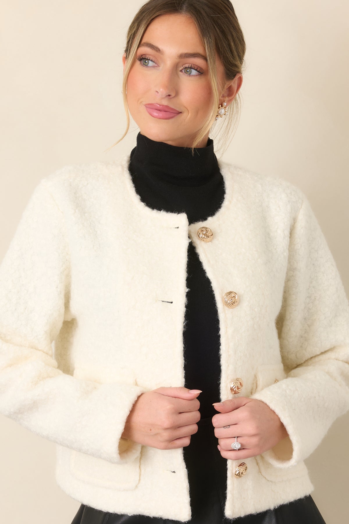Cream bouclé jacket detail highlighting the round neckline and gleaming gold button closures.