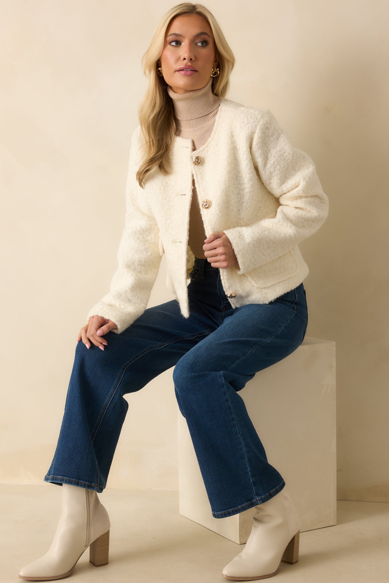 Cream bouclé jacket with a round neckline, long sleeves, front flap pockets, and gold button closures.