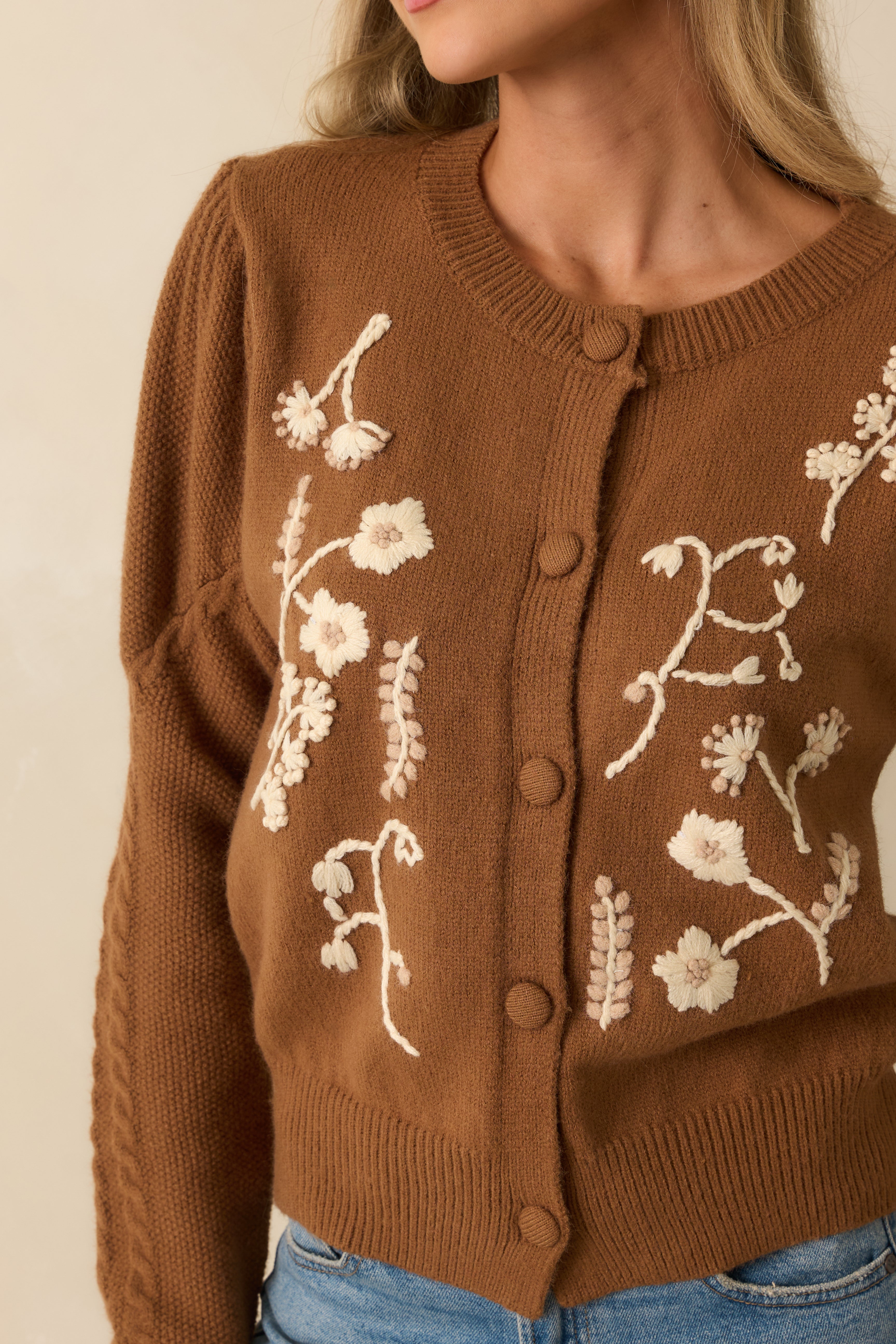 Close-up of the cream floral embroidery and ribbed trim along the crew neckline and hem.