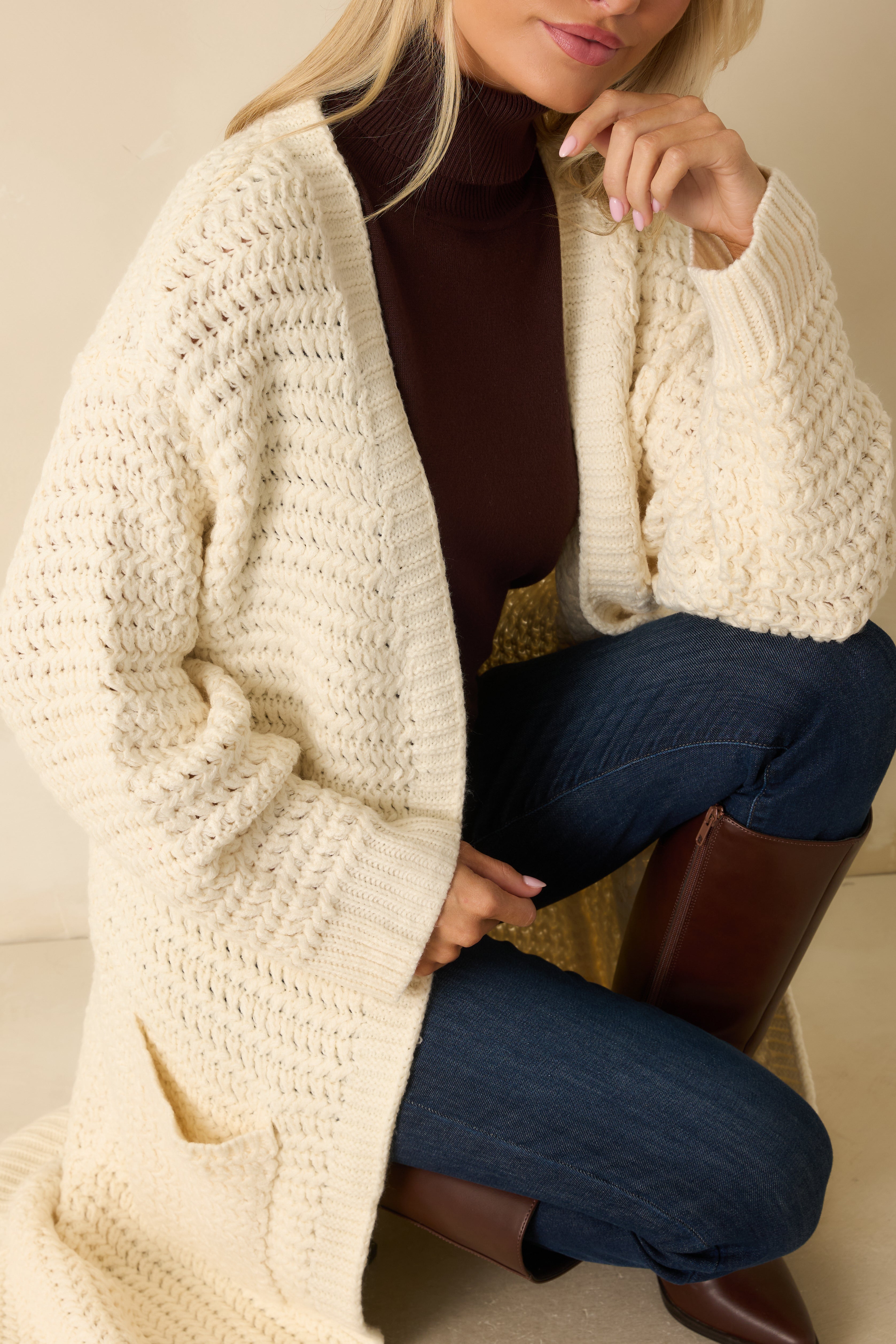 Close-up of the cream knit duster cardigan highlighting the front patch pocket and textured chunky knit pattern.