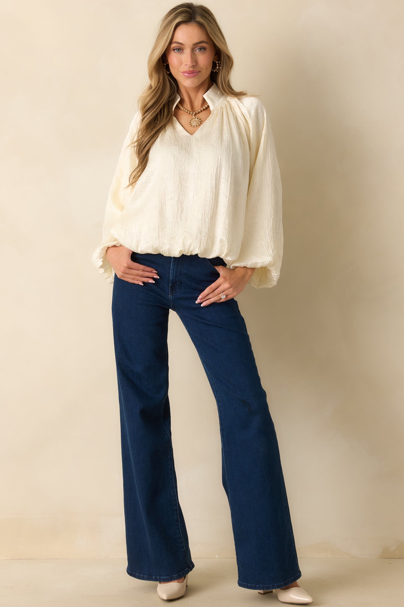 Elegant cream satin blouse with long sleeves, gathered cuffs, and a softly ruched V-neck for gentle shaping.