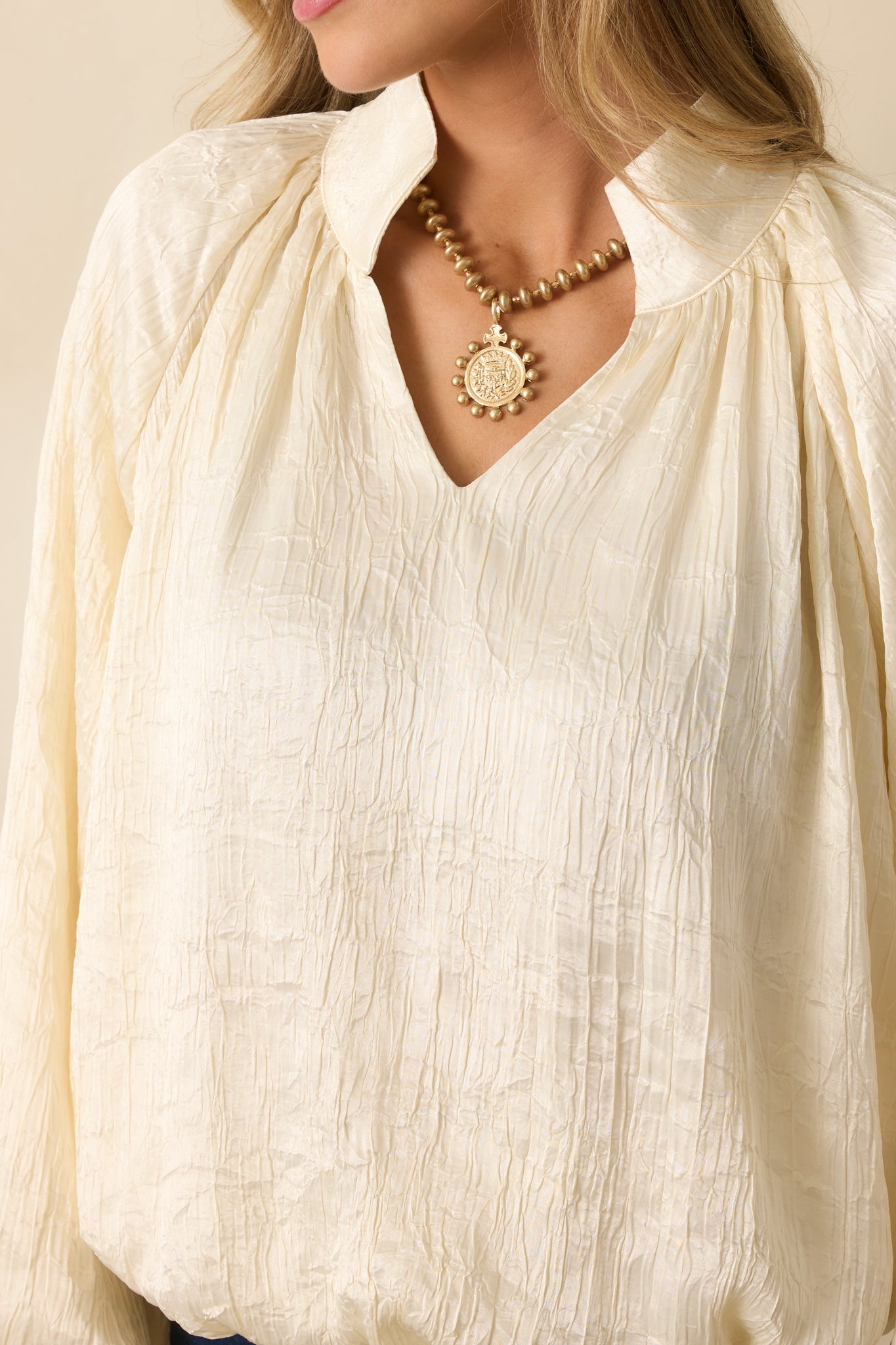 Detailed shot of the cream satin top showcasing the ruched V-neckline, gathered sleeve cuffs, and textured satin fabric.