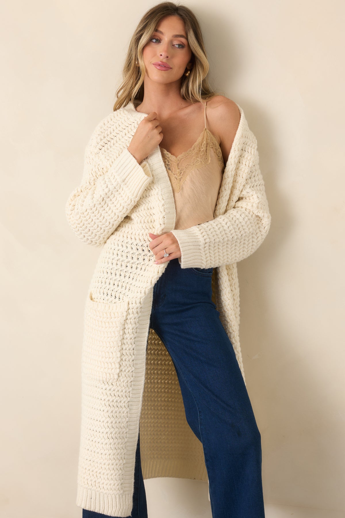 Textured cream cardigan featuring an extra-long shape, ribbed cuffs, and practical front patch pockets.