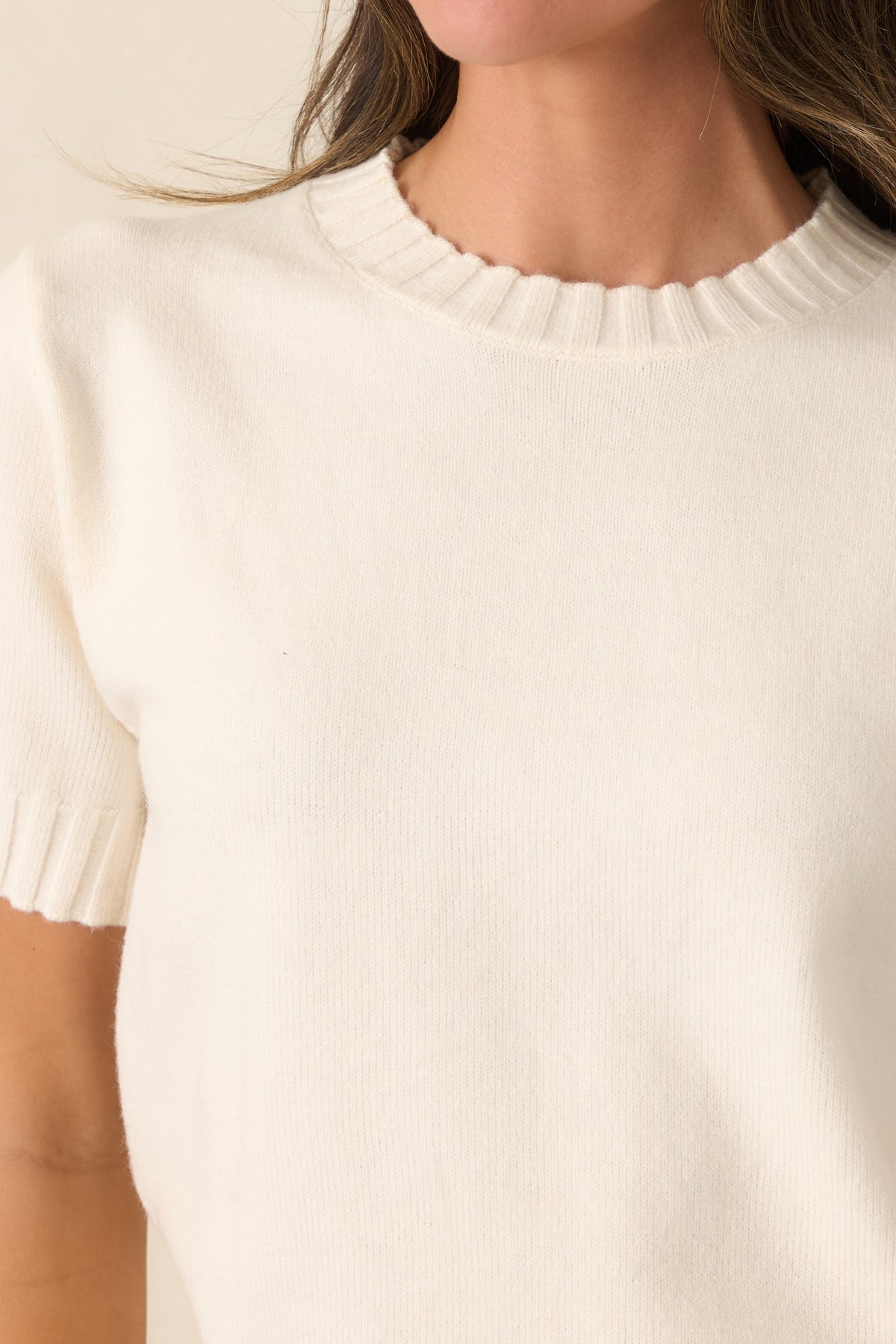 Close-up of the creamy ivory knit top highlighting the crew neckline and textured ribbed trim.