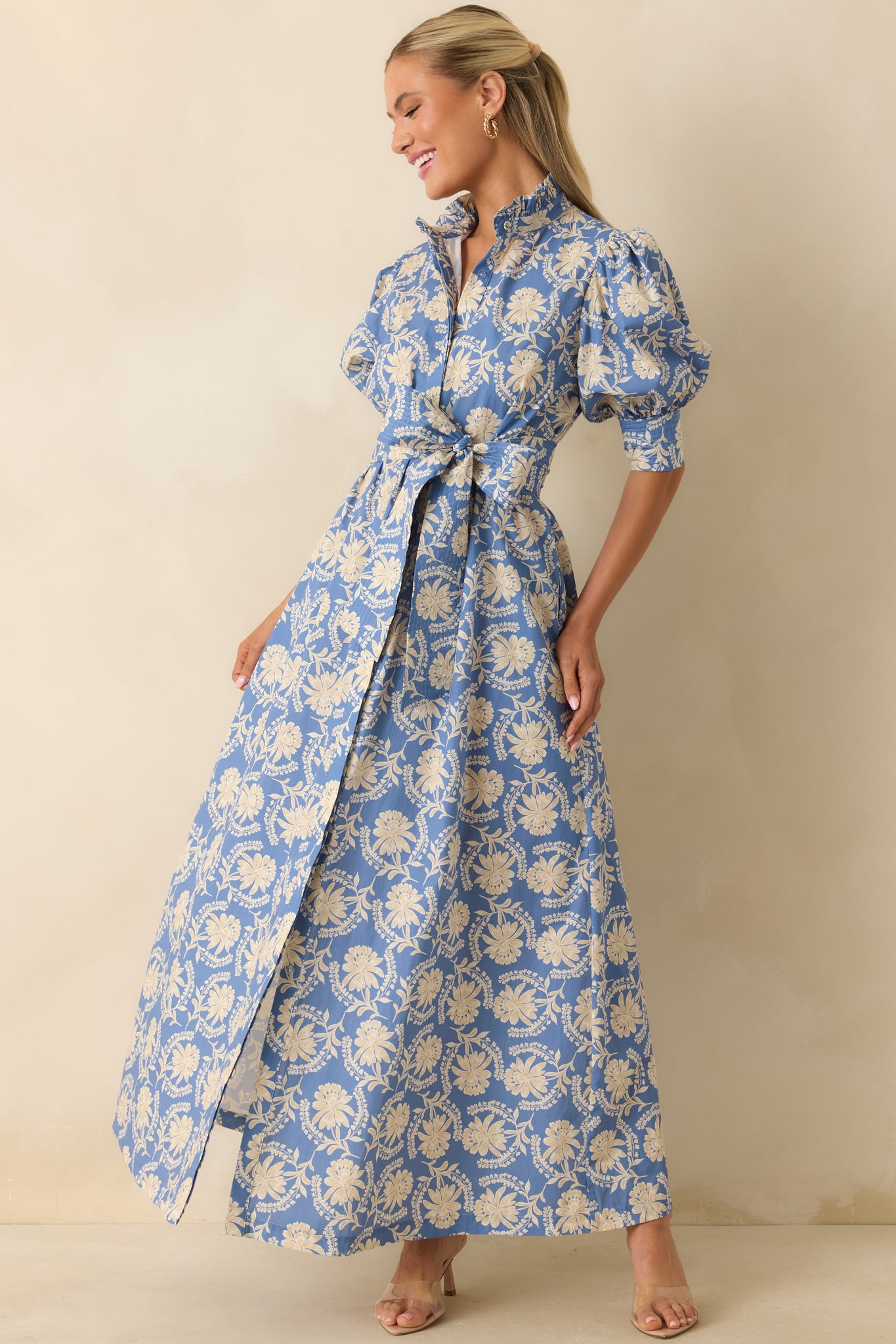 Crisp cotton maxi dress featuring a dusty blue and ivory floral print, a defined self-tie waist, puff sleeves with smocked cuffs, and a flowing full-length skirt.