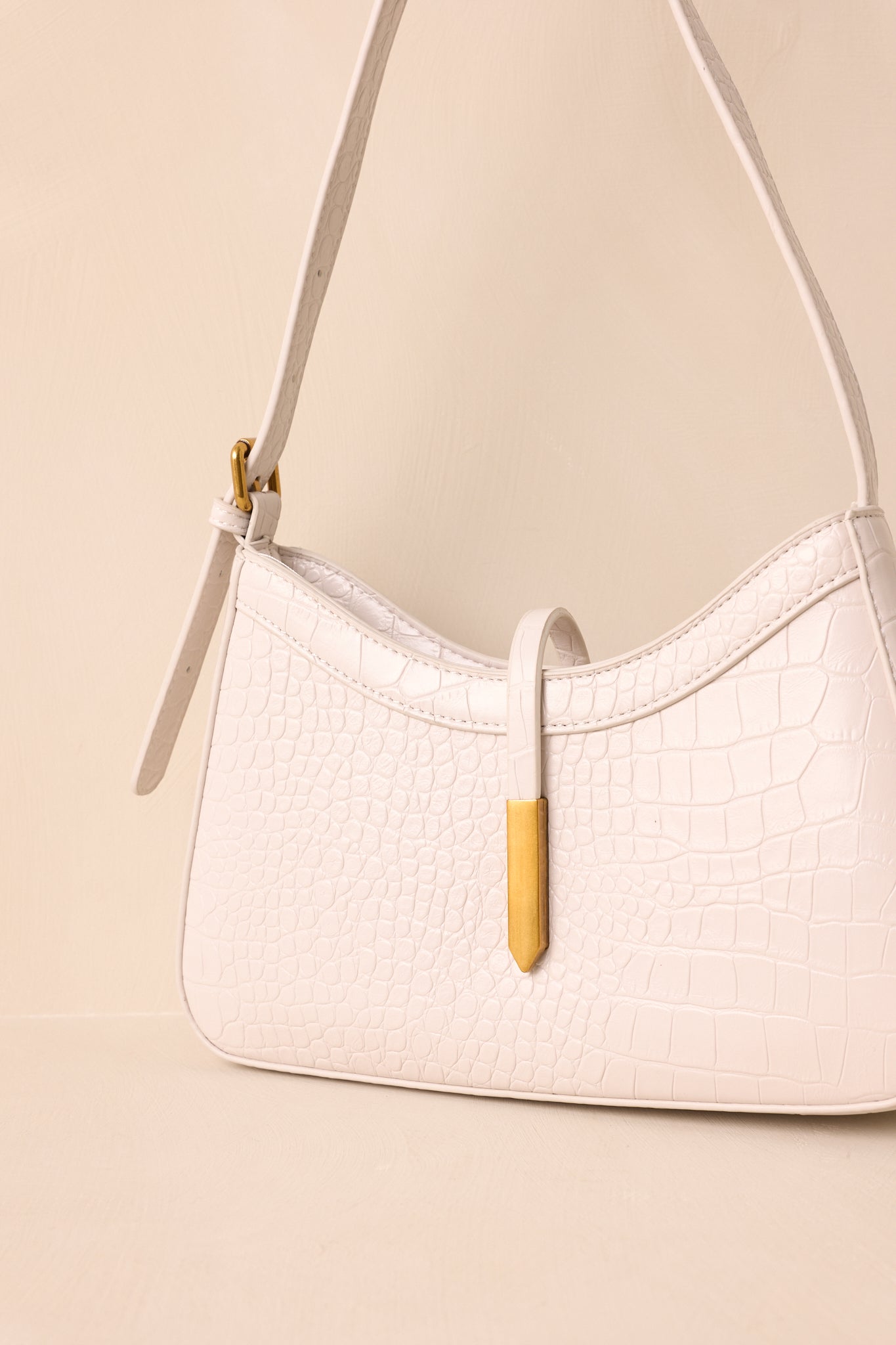 Close-up of croc-embossed faux leather and gold hardware, focusing on rectangular strap closure tip.