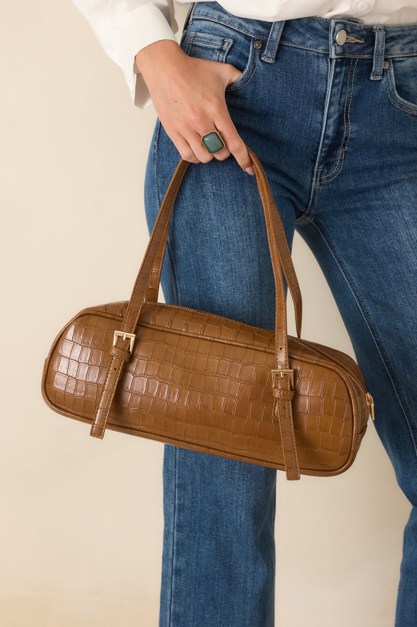 Close view of the handbag highlighting the croc-embossed texture, elongated shape, and refined faux leather finish.