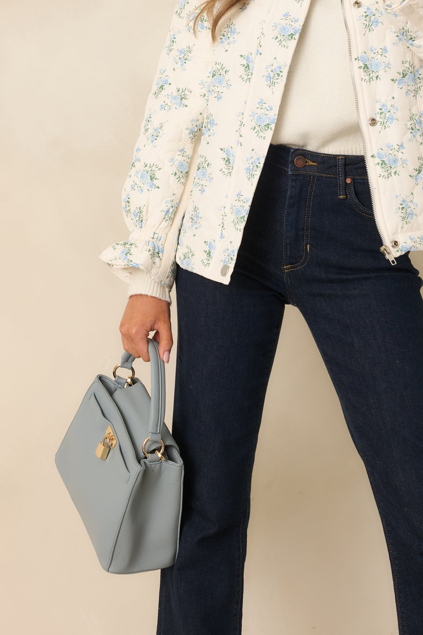 Cropped angle emphasizing the decorative lock and top handle on the dusty blue structured handbag.