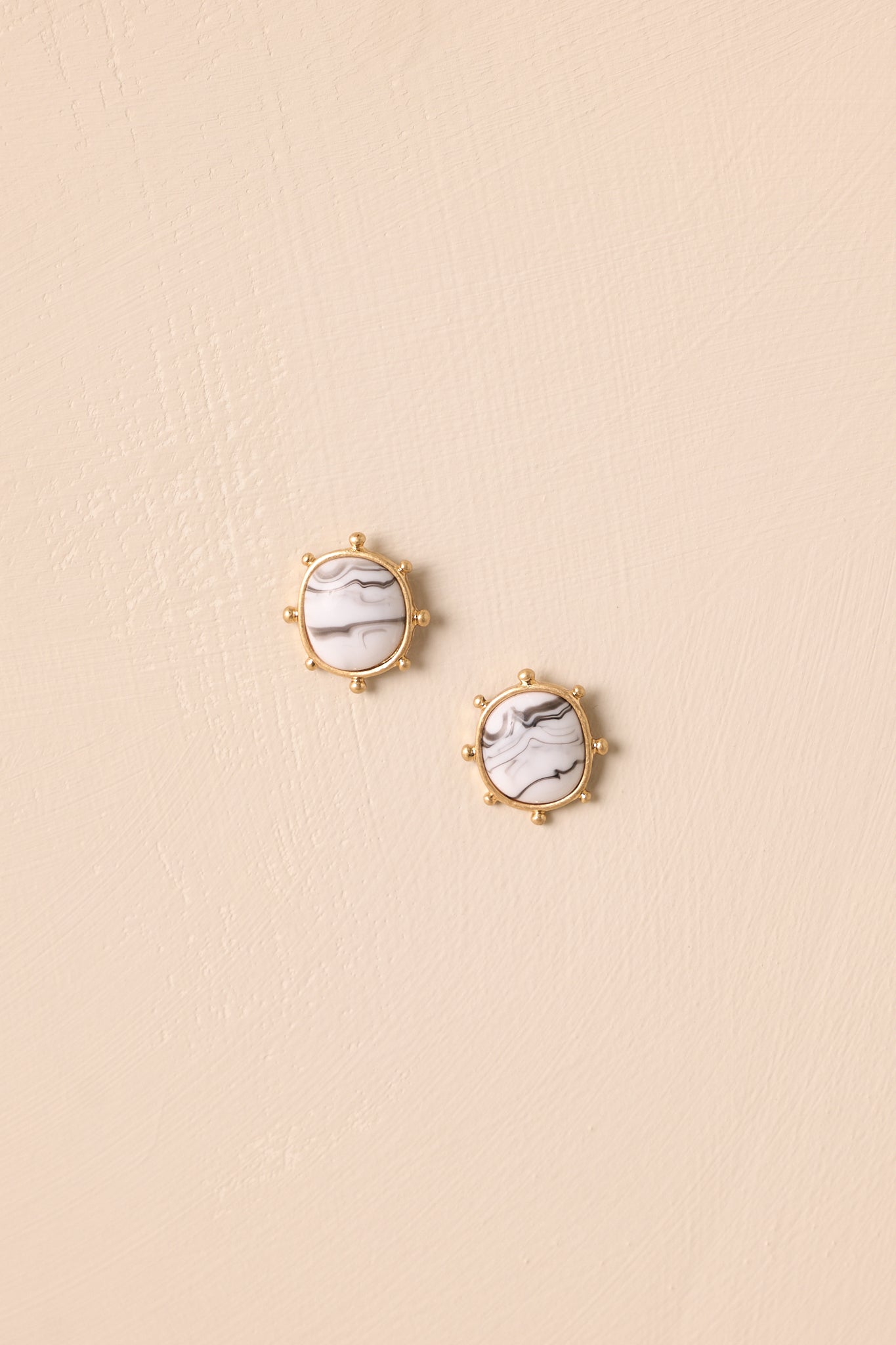 A close-up cropped shot highlighting the decorative gold ball prongs around the marble stone earrings.