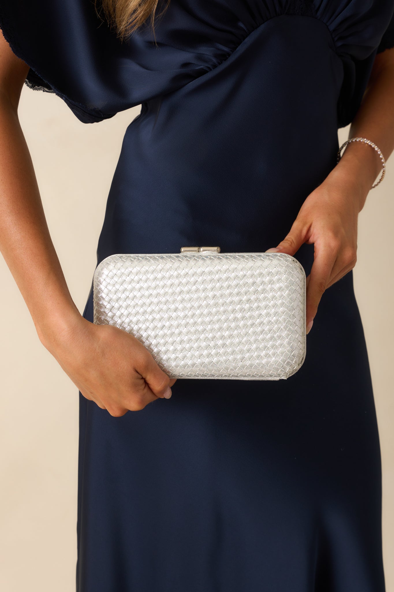 A cropped angled shot of the clutch focusing on the hinged frame and metallic woven texture.