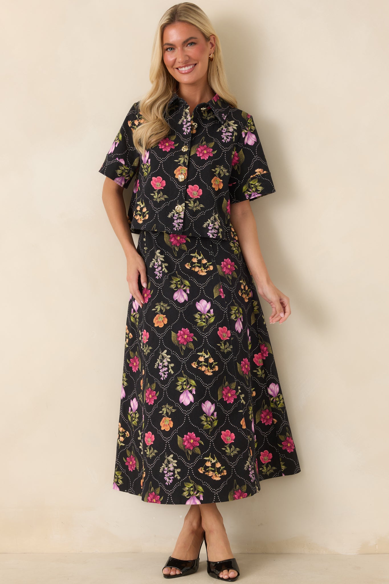 Cropped black top featuring colorful floral motifs, a dotted lattice print, and sculptural gold-tone buttons.