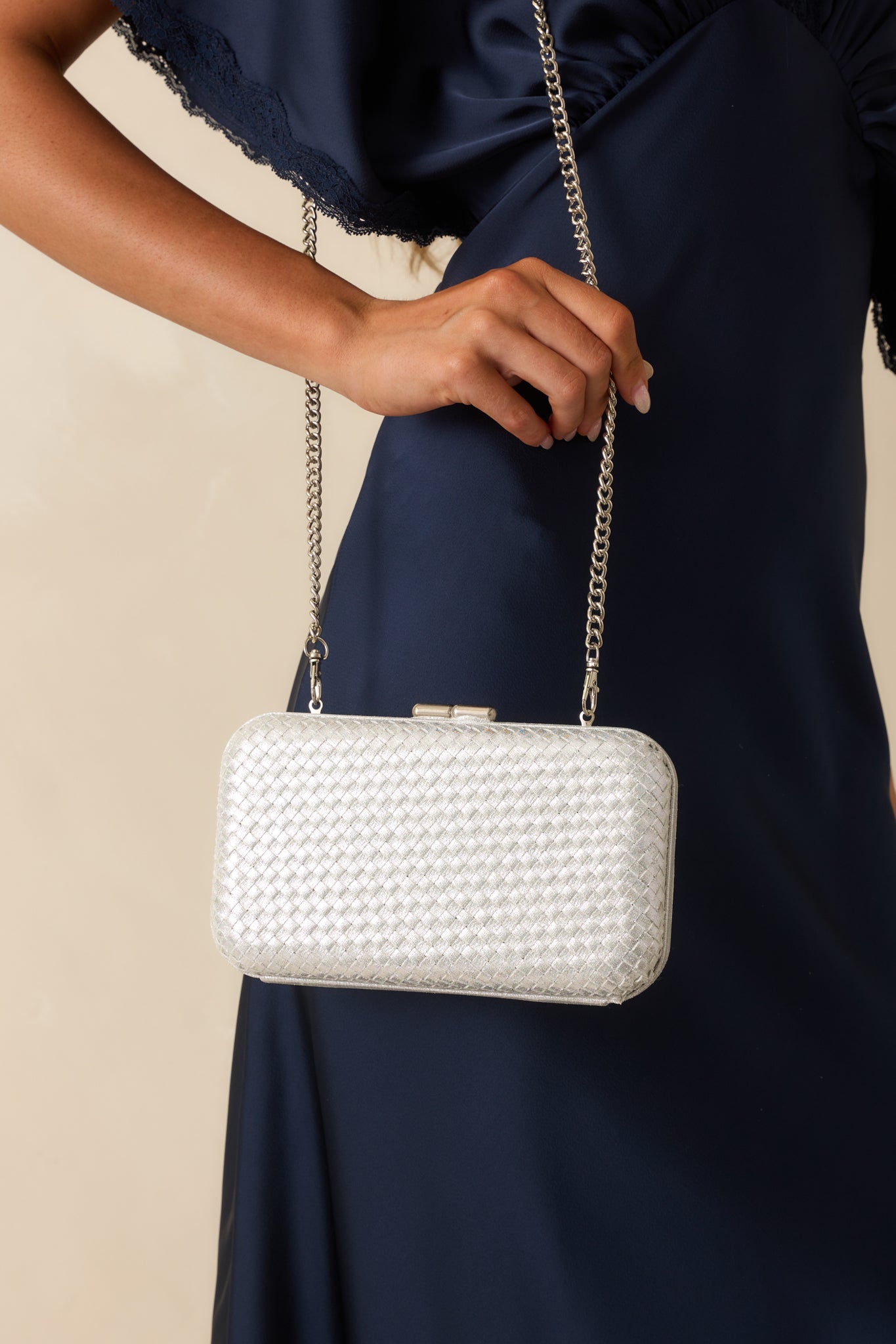 A cropped close view of the silver clutch showing the optional chain strap attached at the sides.