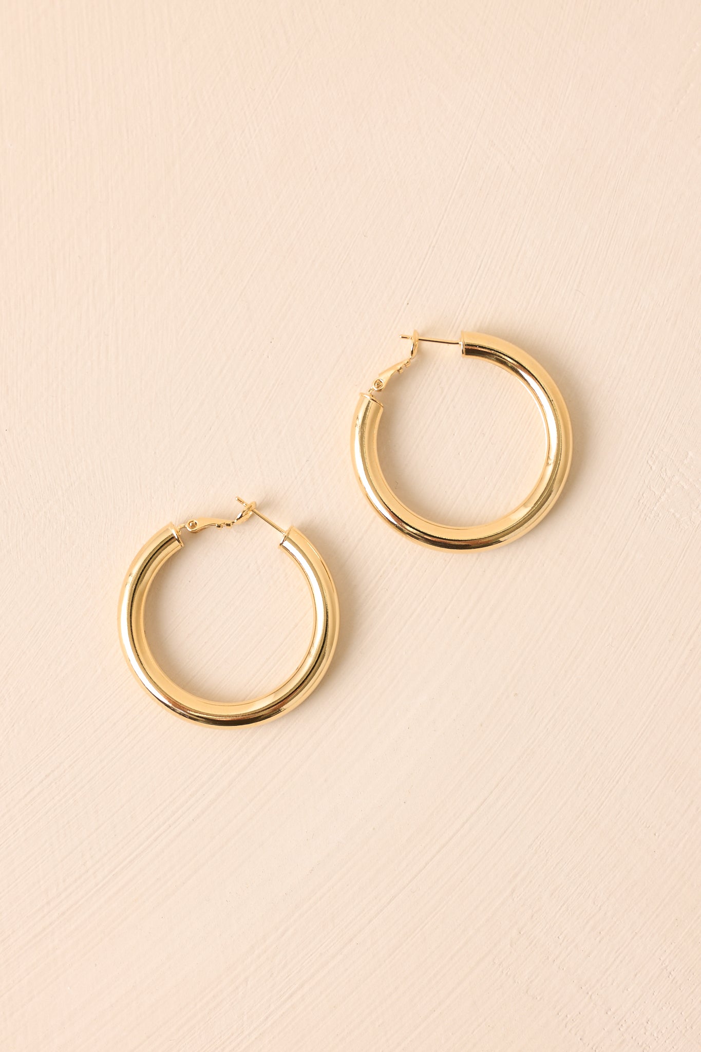 Cropped close view of the gold hoop earrings highlighting their medium size and curved silhouette.
