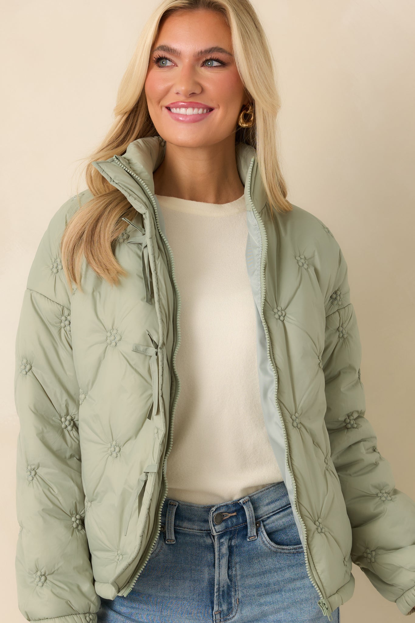 Cropped detail emphasizing the stand collar and elasticized cuff on the sage green quilted puffer jacket.