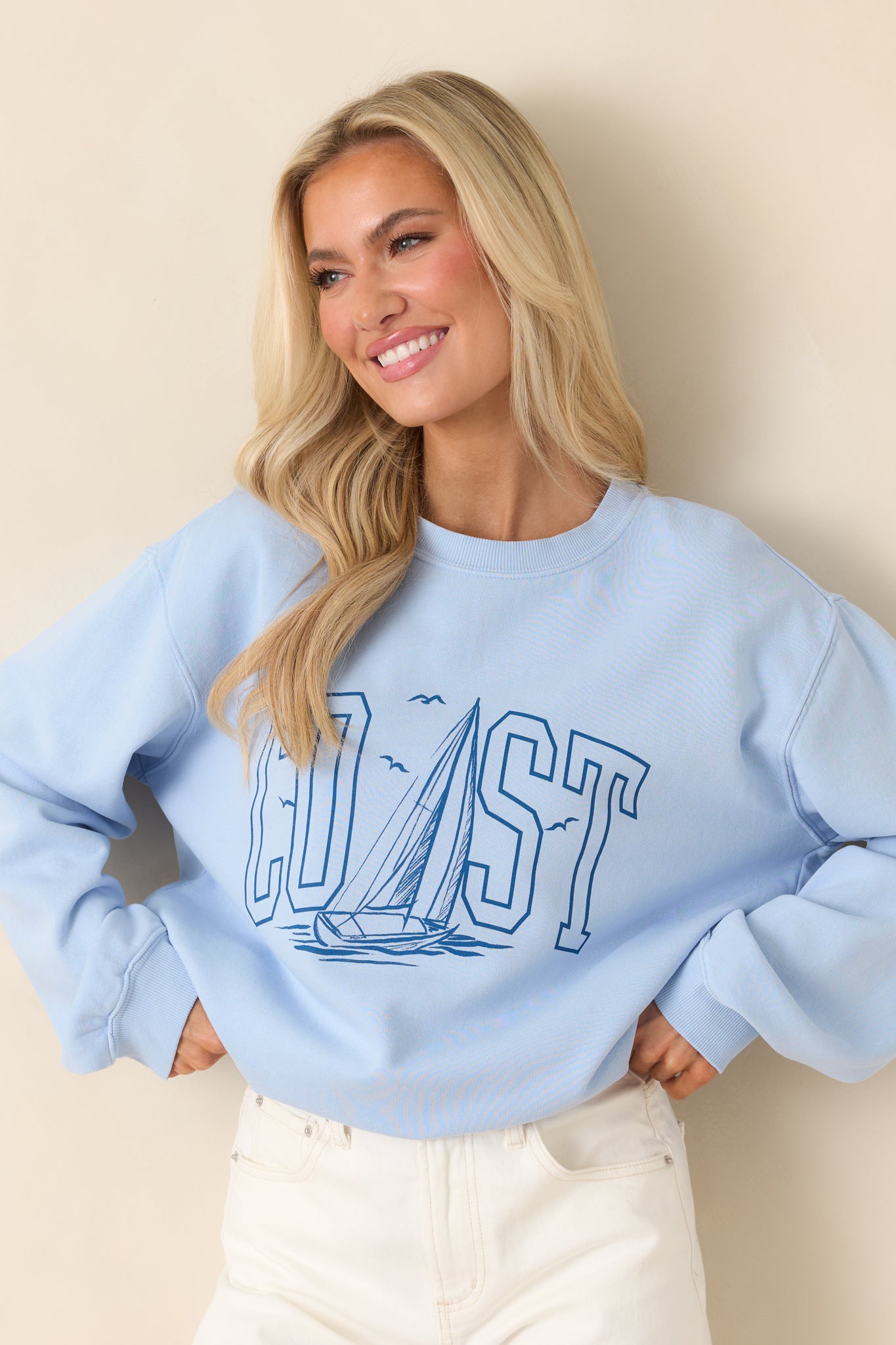 Cropped front view highlighting the “COAST” graphic and nautical-inspired sailboat illustration on the light blue sweatshirt.