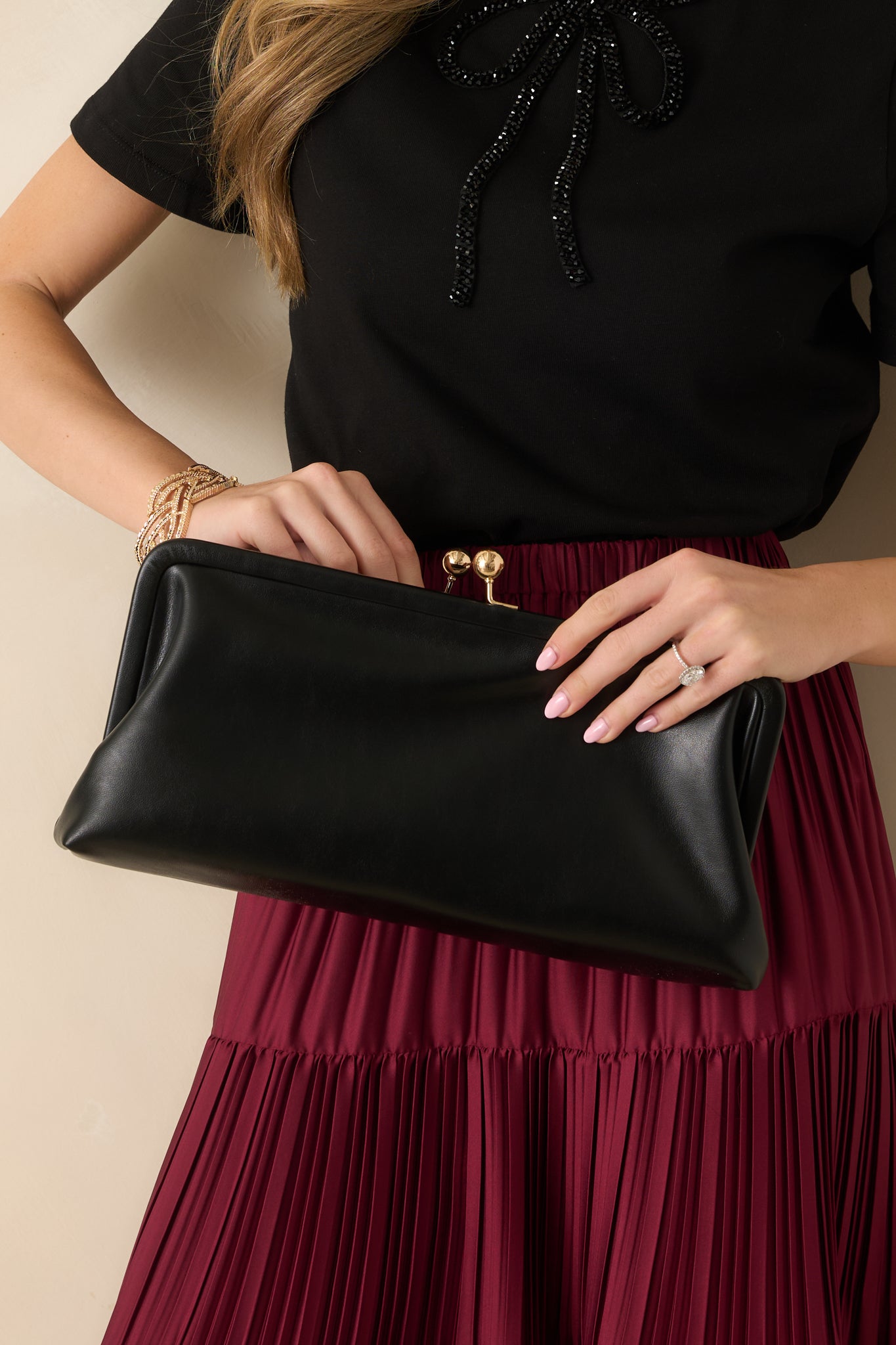 Cropped front view focusing on the gold-tone kiss-lock closure and smooth black faux leather exterior.