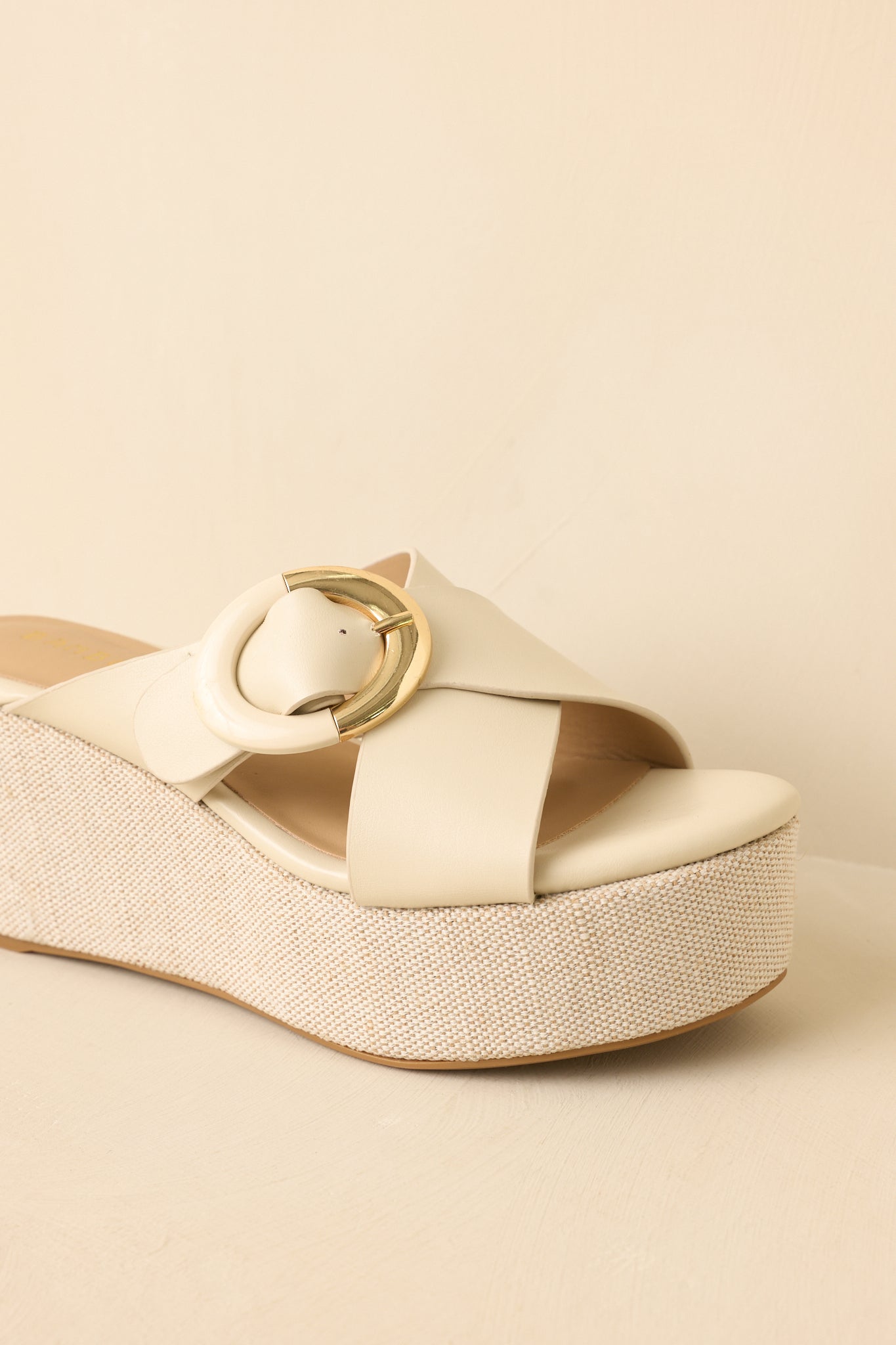 Cropped front-side view of ivory platform wedges showcasing the soft neutral tone and bold buckle accent.
