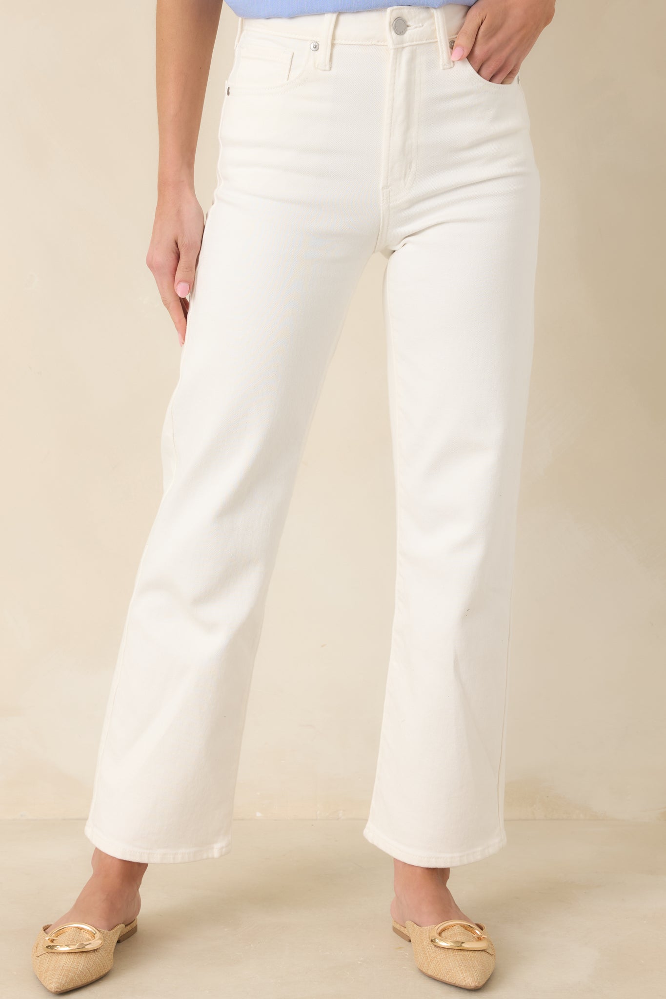 Cropped front detail of white jeans showcasing the metal button and zipper fly closure.