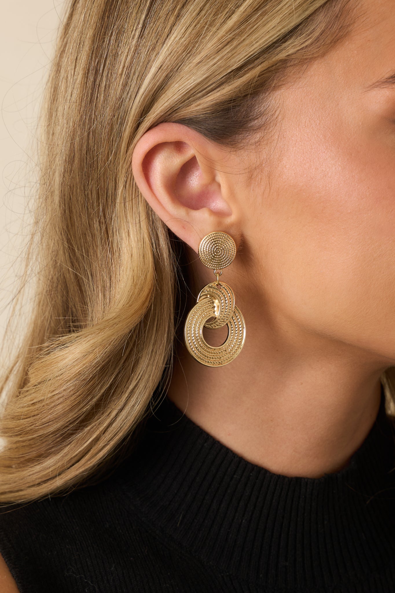 Cropped view of gold drop earrings featuring double interlocked circular drops with a thread-like textured finish.