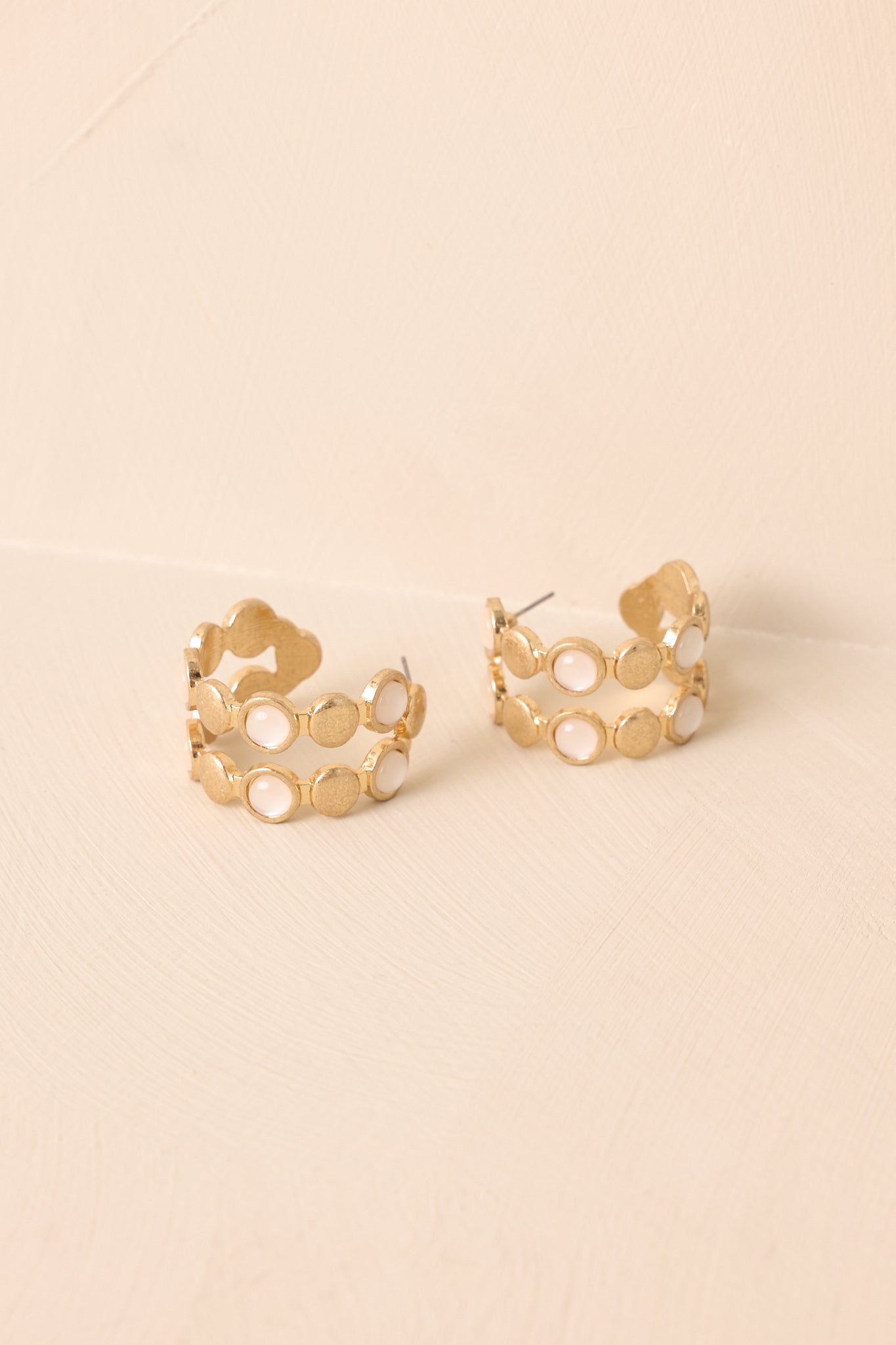 A cropped view of the gold open hoop earrings with circular discs and iridescent stone accents.
