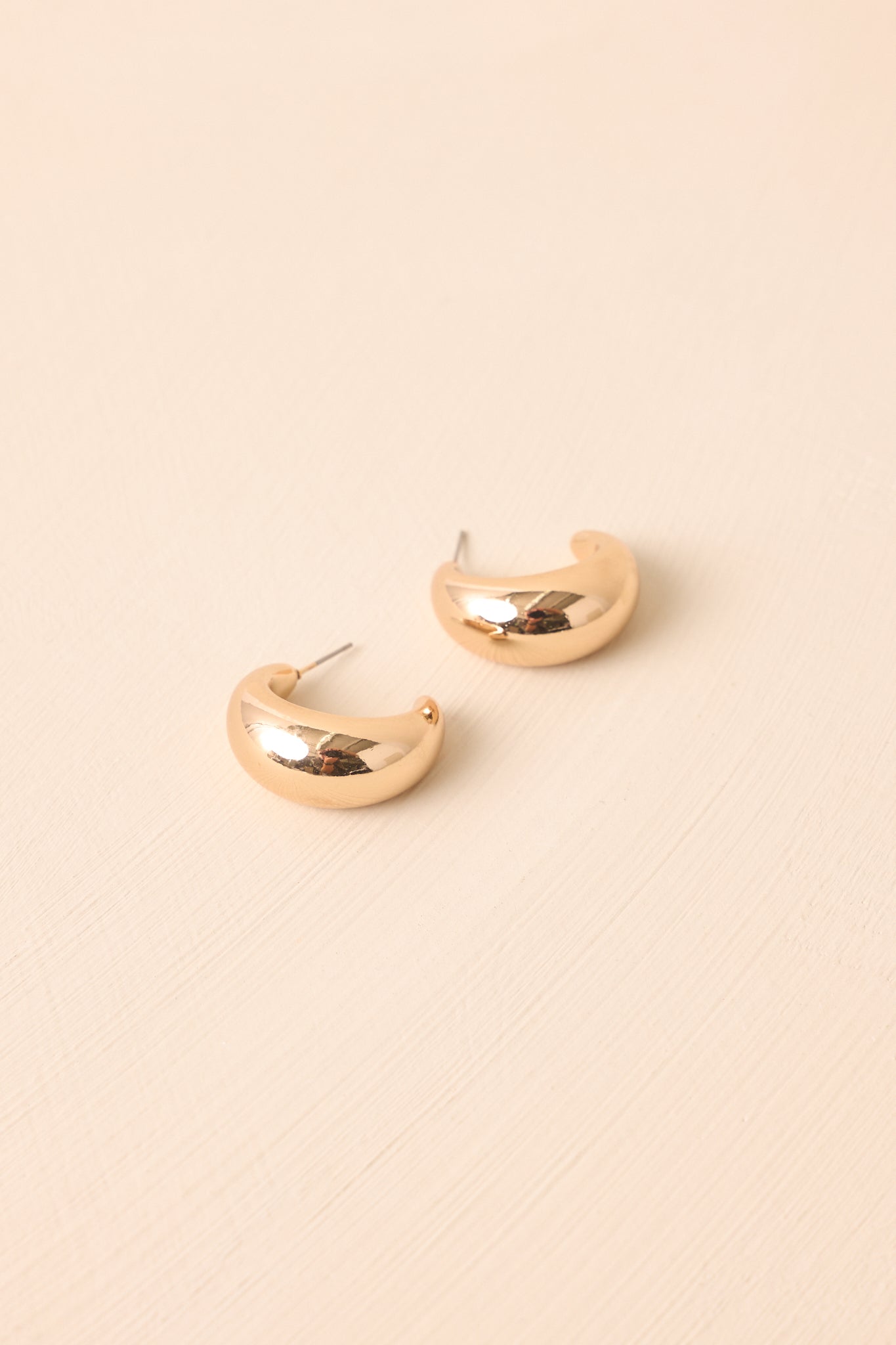 A close-up cropped shot highlighting the smooth polished surface of the gold dome hoop earrings.
