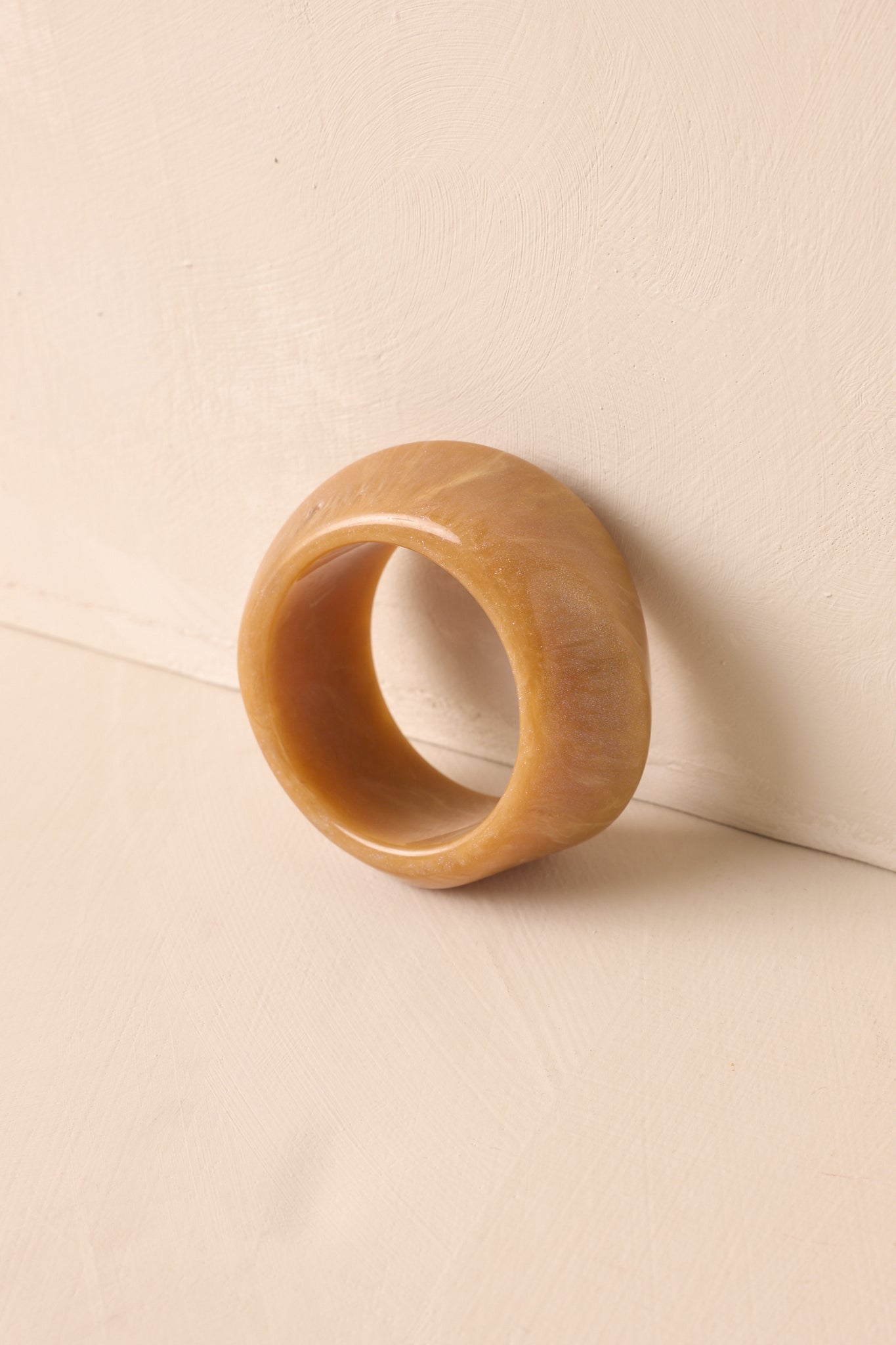 A cropped view of the wide tan marbled acrylic bangle with a twisted textured design.