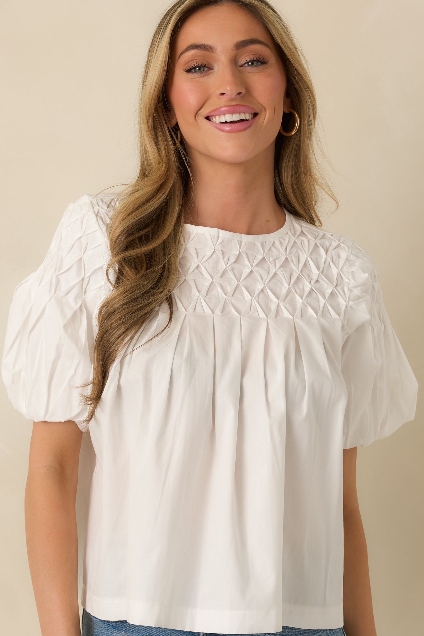 Cropped front view of a white top emphasizing the lattice smocked yoke and round neckline detail.