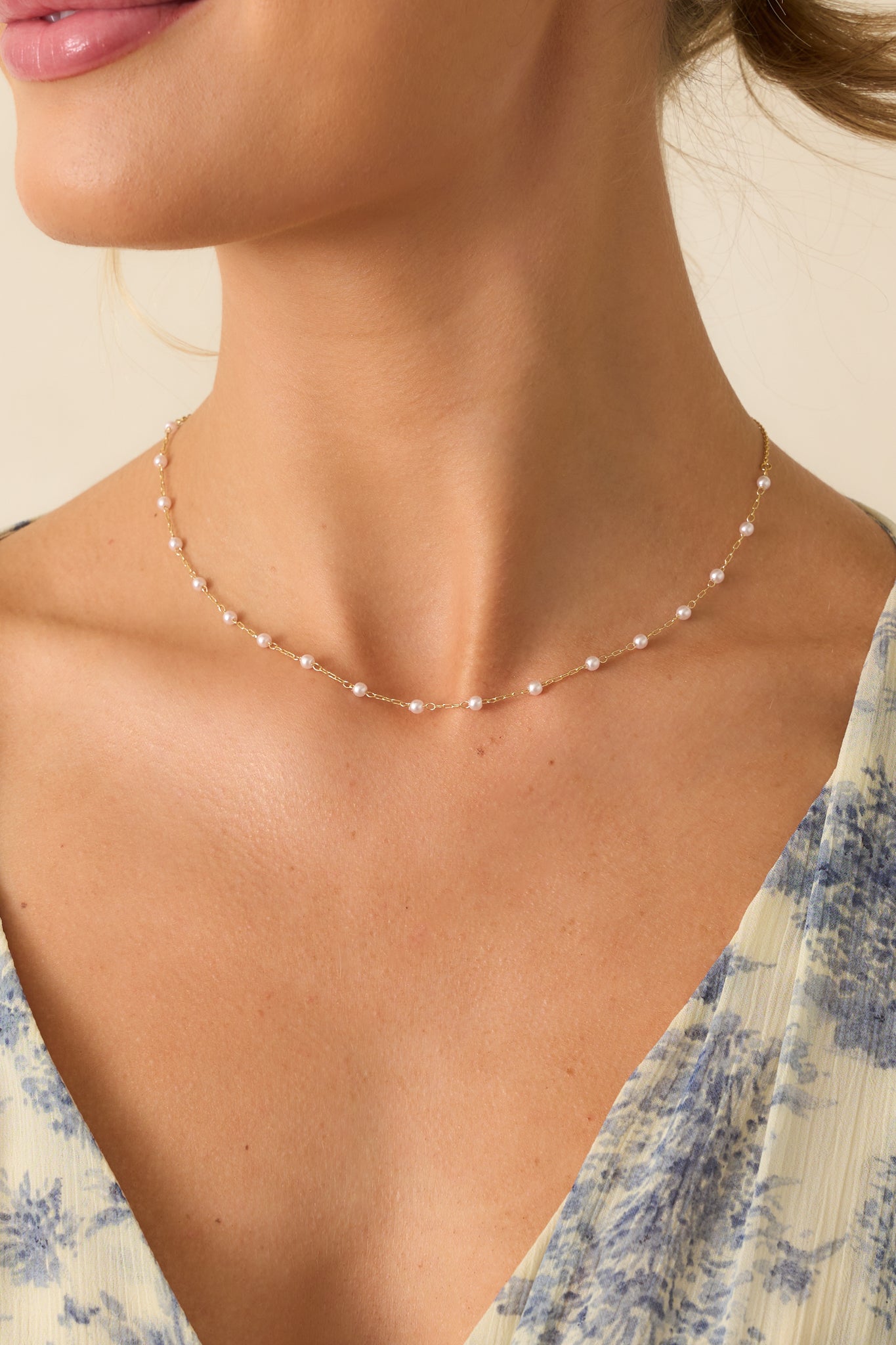 Cropped view of the gold and ivory pearl necklace, highlighting the small faux pearls patterned along the thin gold rectangular and circle chain.