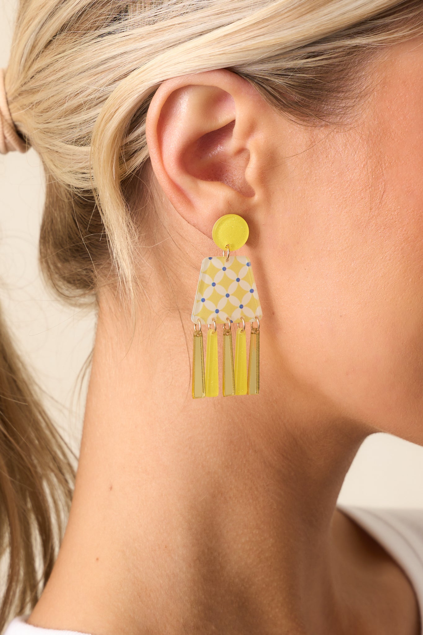 Tightly framed view of the earring highlighting the gold jump rings and layered gold and yellow acrylic dangles.