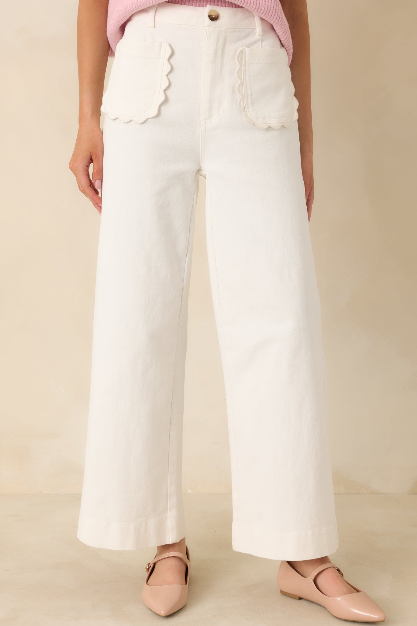 Close cropped view highlighting the scalloped trim on the front patch pockets of ivory pants.