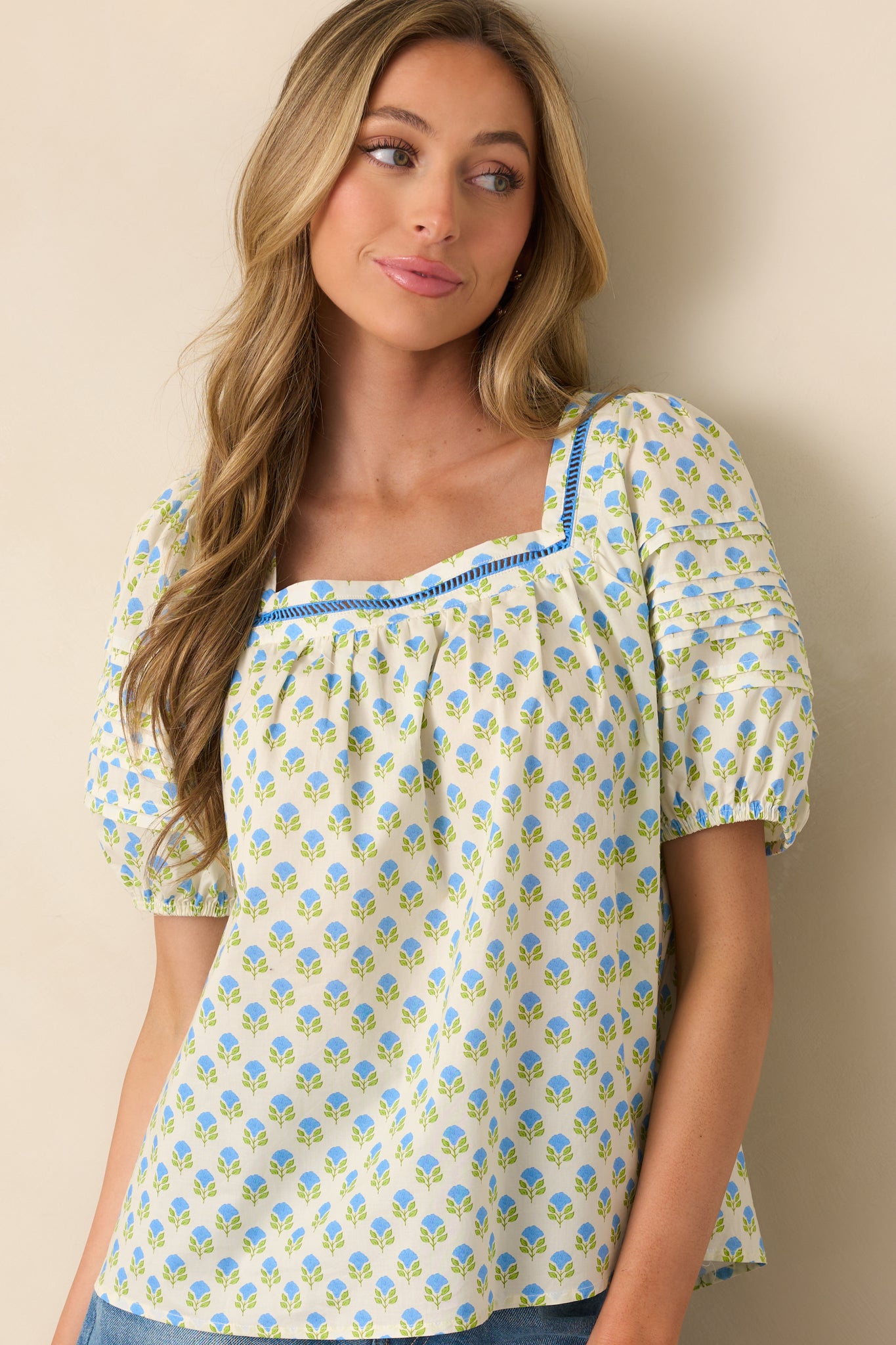 A cropped view highlighting the detailed ladder lace trim around the square neckline of the blue floral printed top.
