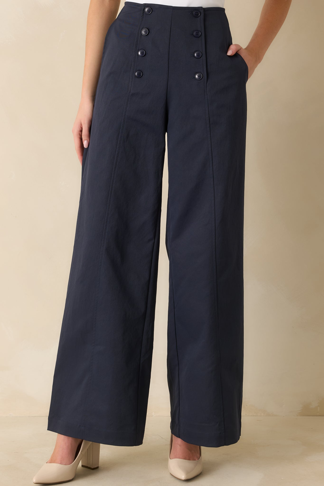 Cropped view of navy pants’ waist and upper legs highlighting front button closures and high-rise fit.
