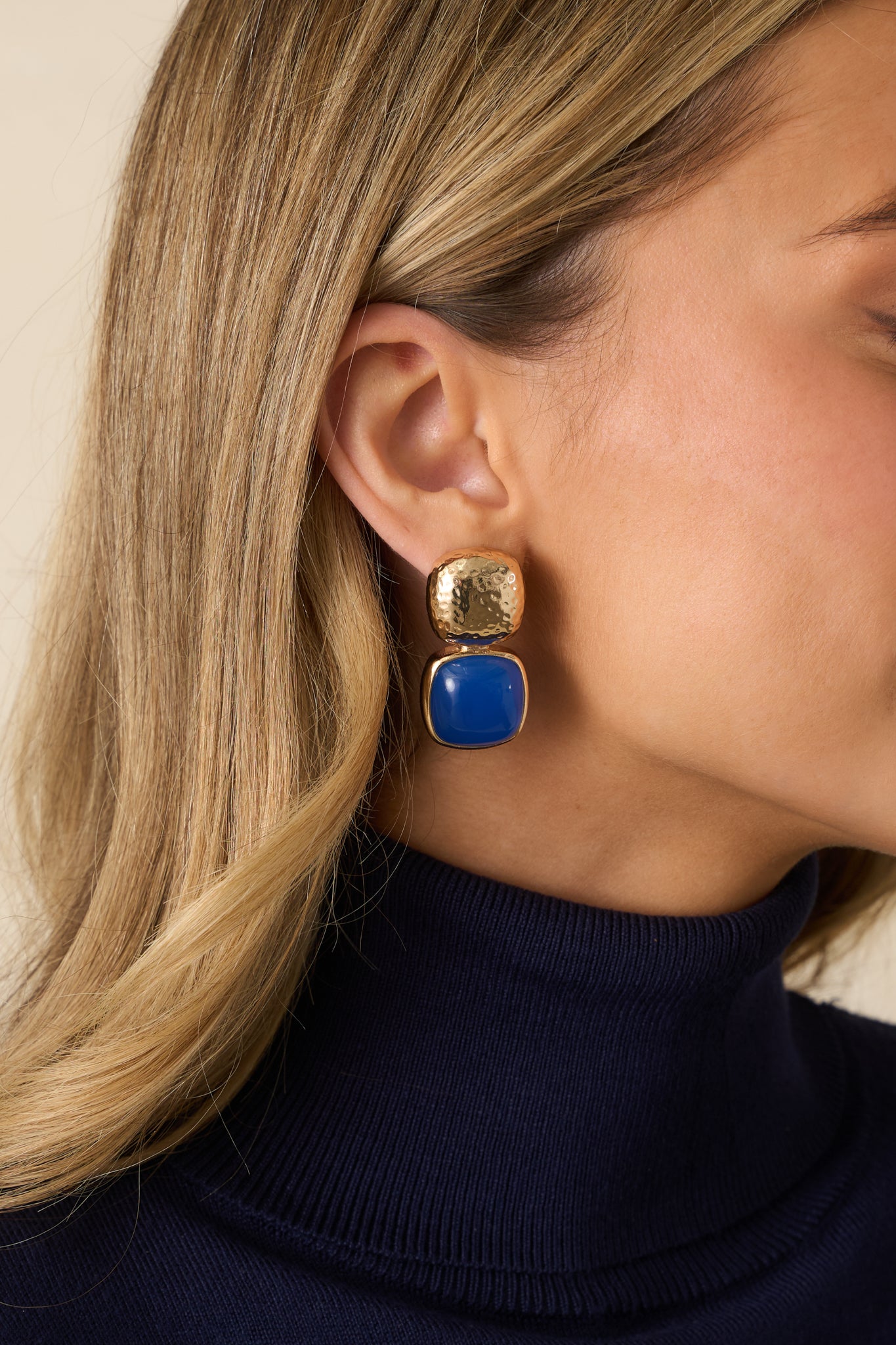 Cropped view of blue drop earrings featuring a gold textured square stud and a blue square stone.