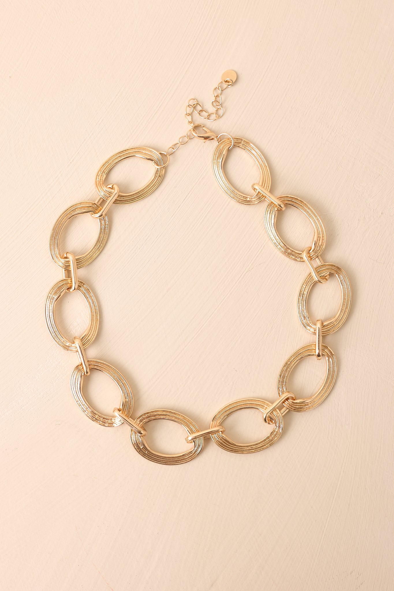 Cropped view of gold necklace with oversized textured oval links and smaller connecting links.