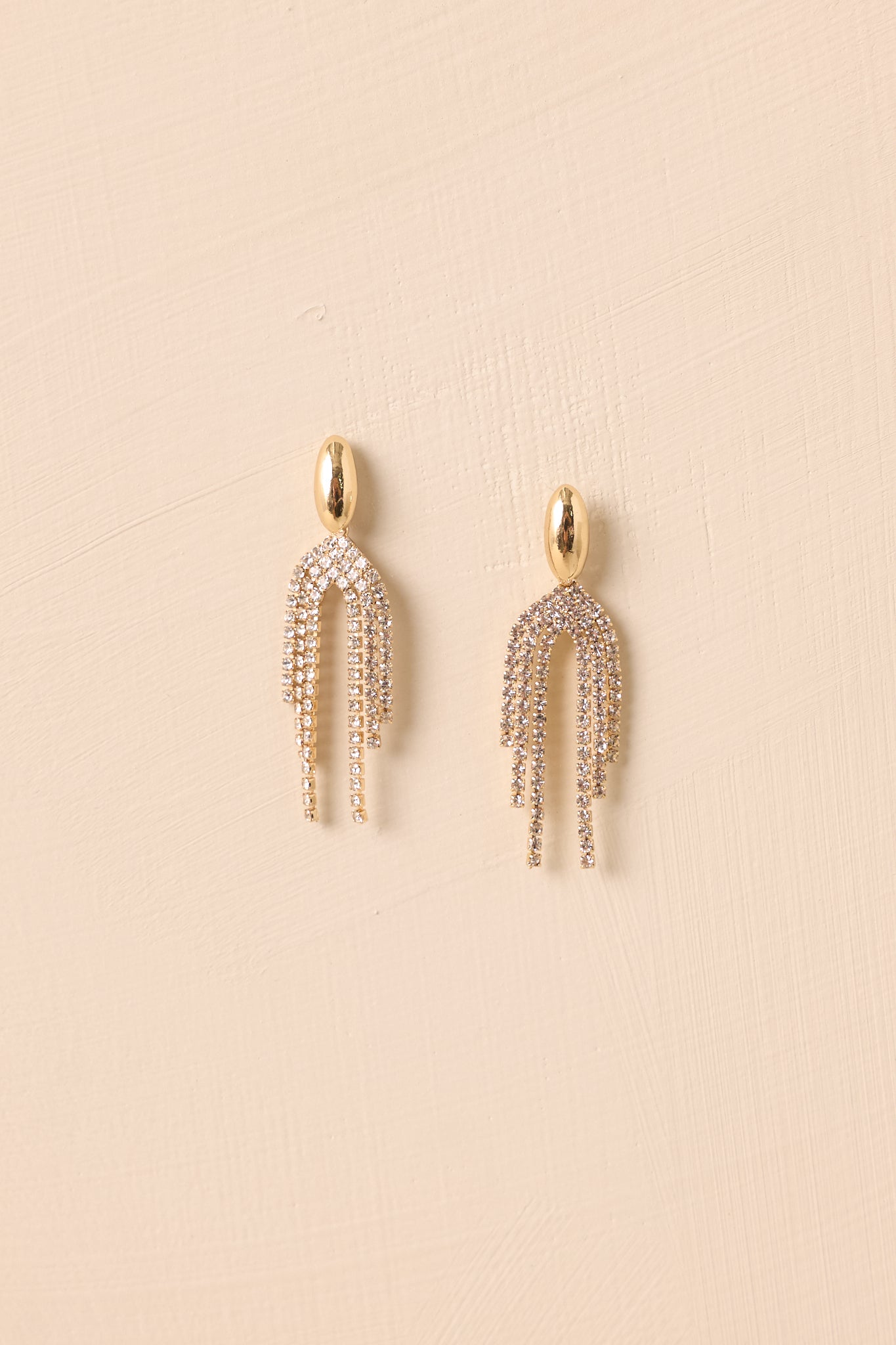 Cropped view of gold oval stud earrings with cascading rhinestone tassel strands.