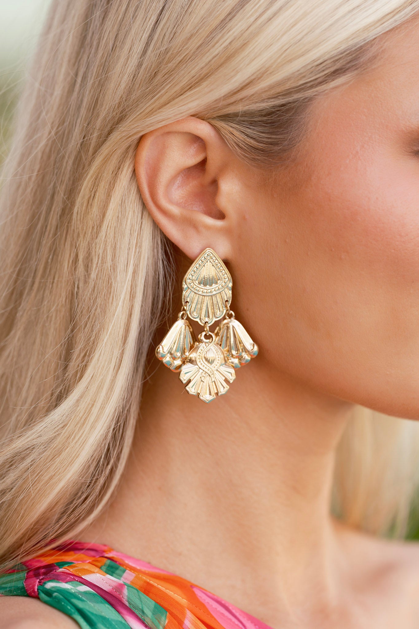 A cropped image highlighting the dangling three-drop charm design of the textured gold chandelier earrings.
