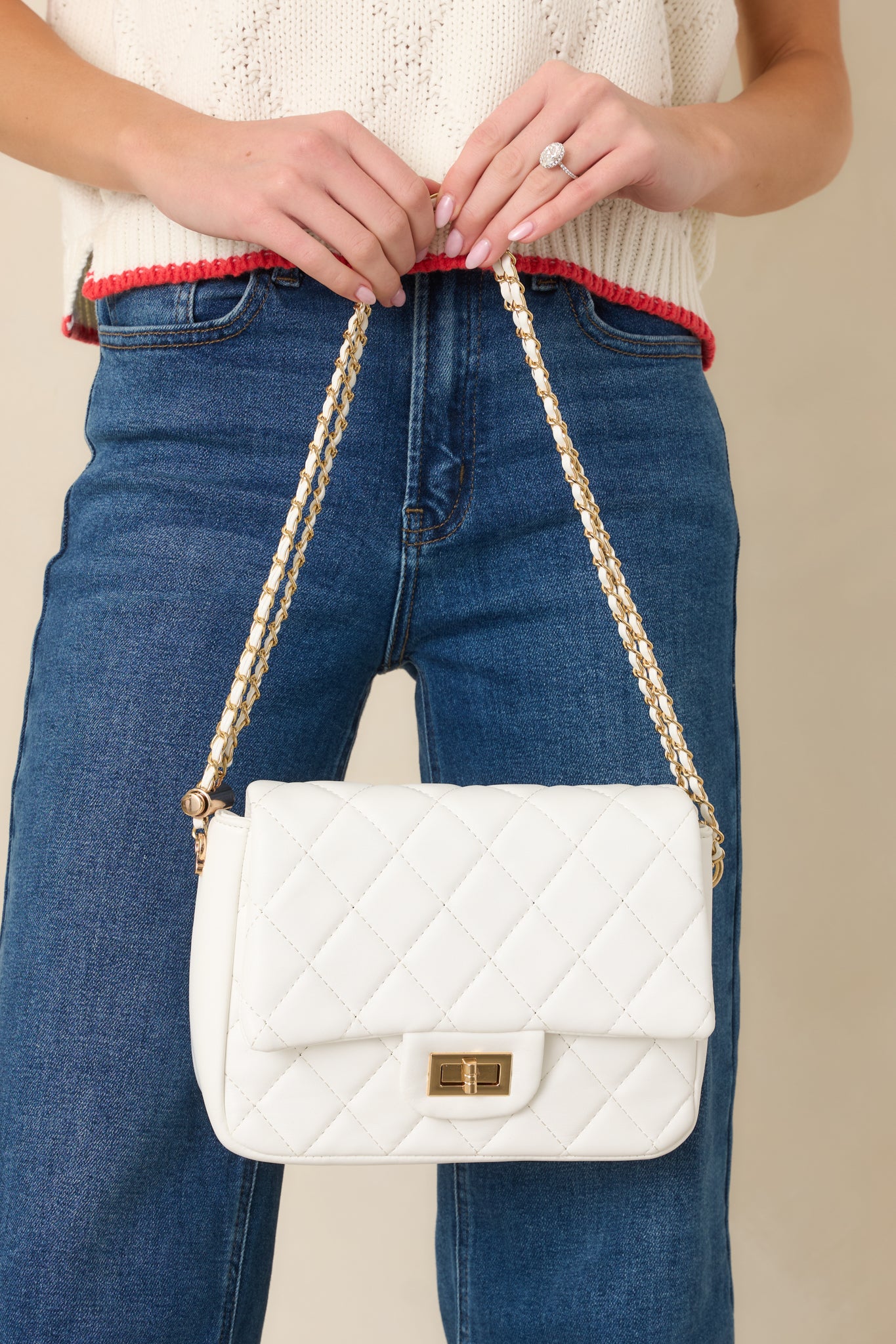 Cropped view of white quilted handbag focusing on gold twist lock closure and chain strap.