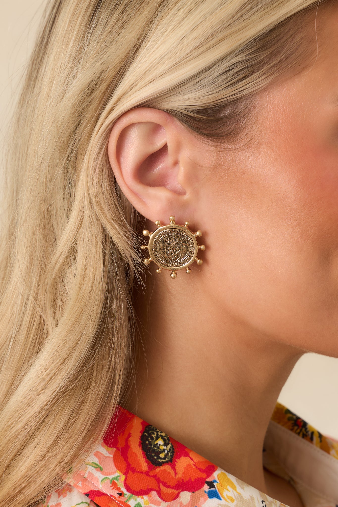 Cropped view of worn gold coin medallion earrings highlighting embossed detailing and ball prong frame.