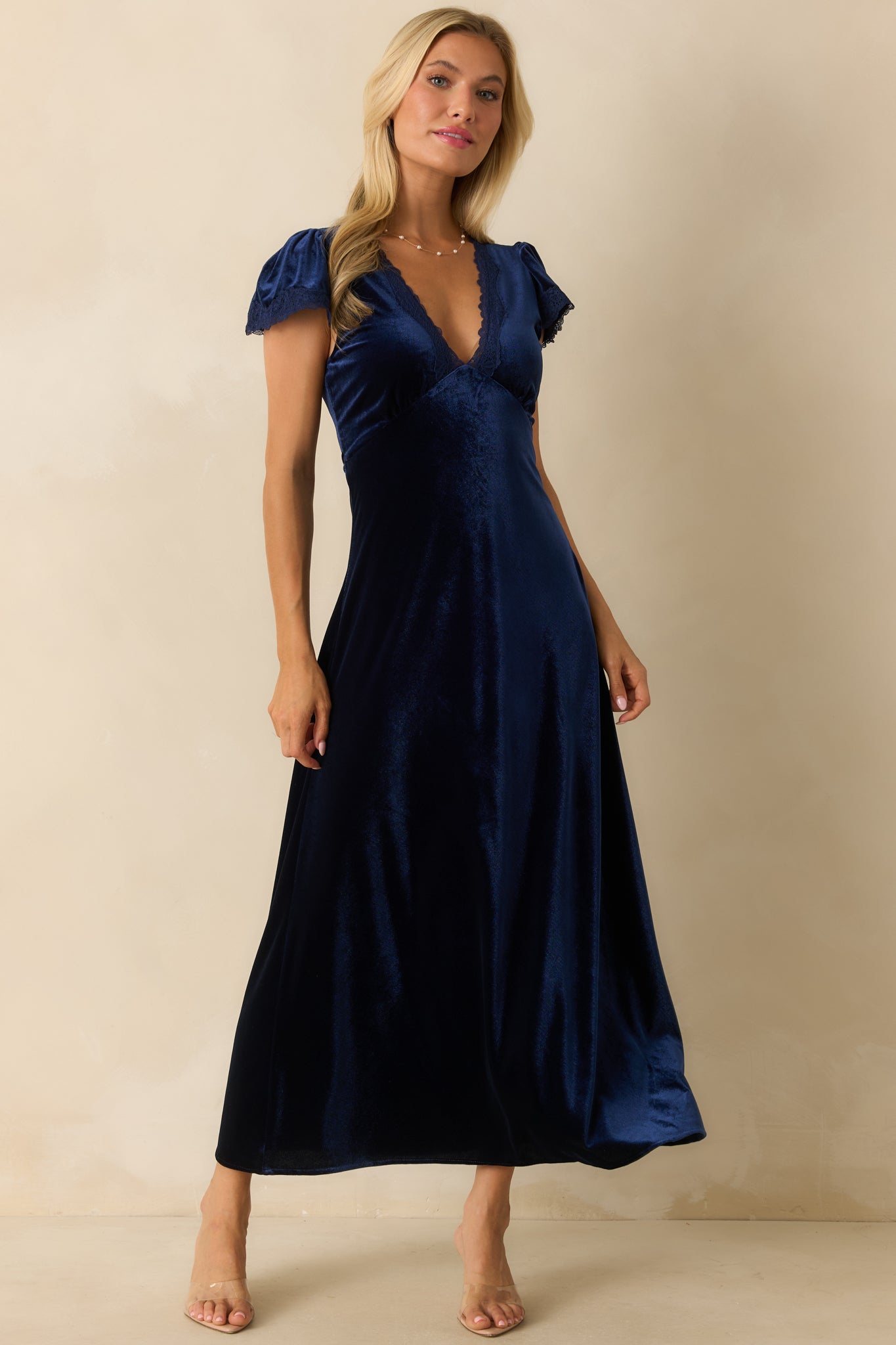 Front view of dark blue velvet dress featuring empire waist, flutter sleeves, and elegant floor-length silhouette.