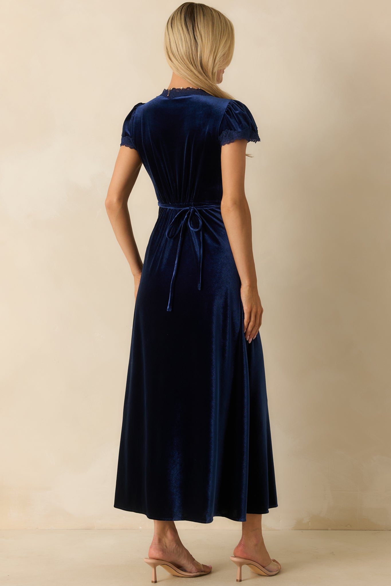 Rear view of dark blue velvet maxi dress showing flutter sleeves, empire waist, and flowing A-line skirt.