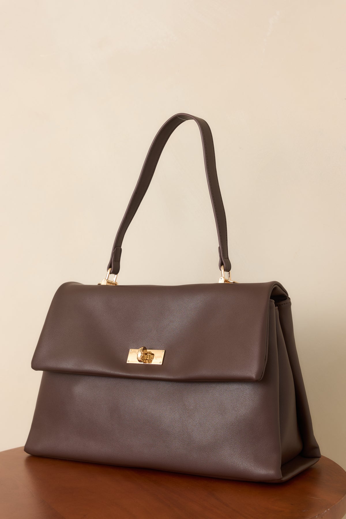 Close-up of the handbag’s gold-tone twist-lock closure against its smooth dark brown faux leather.
